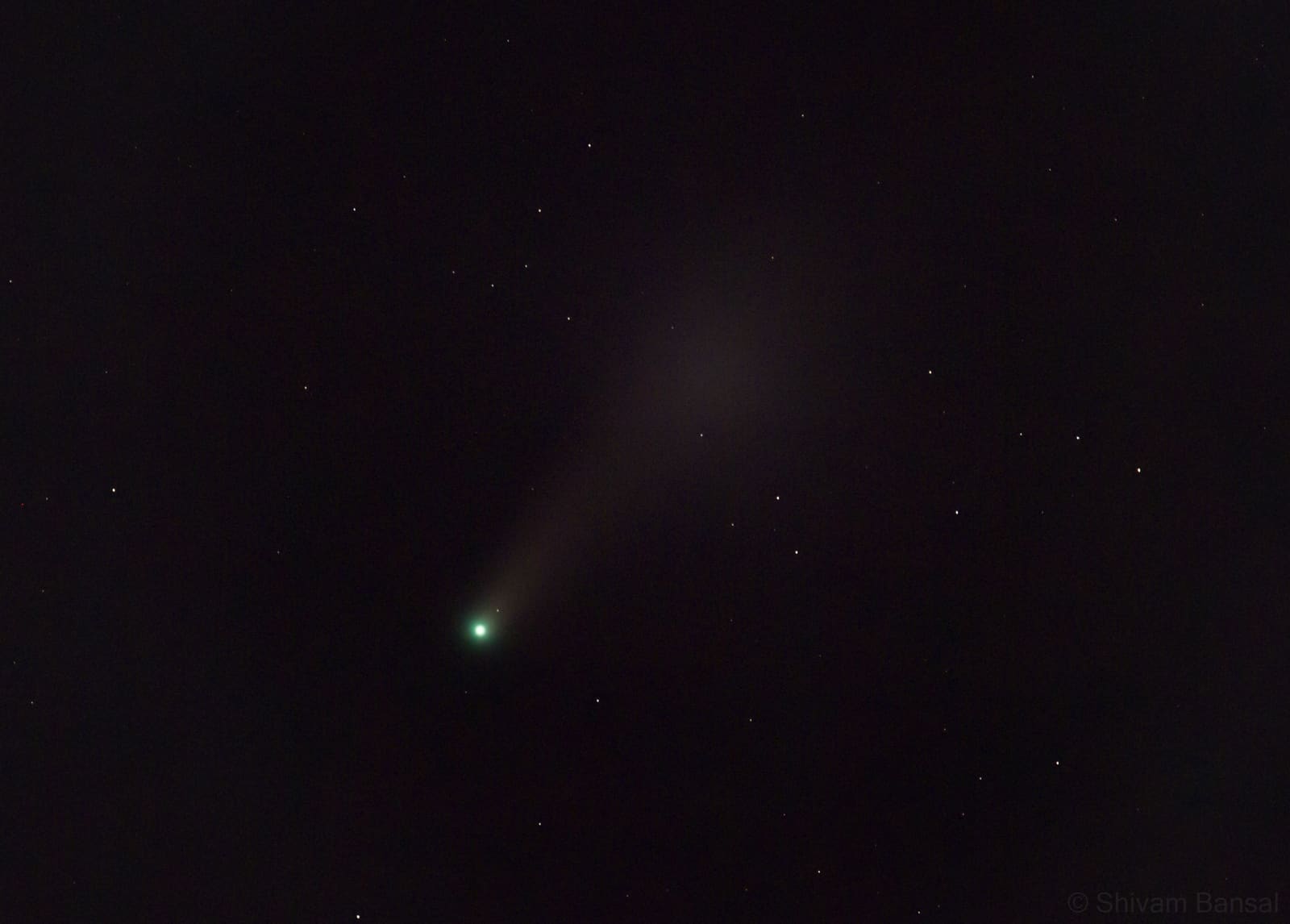 Close telephoto view of Comet NEOWISE showing a bright green nucleus and a soft dust tail fanning diagonally across a dark starry sky.