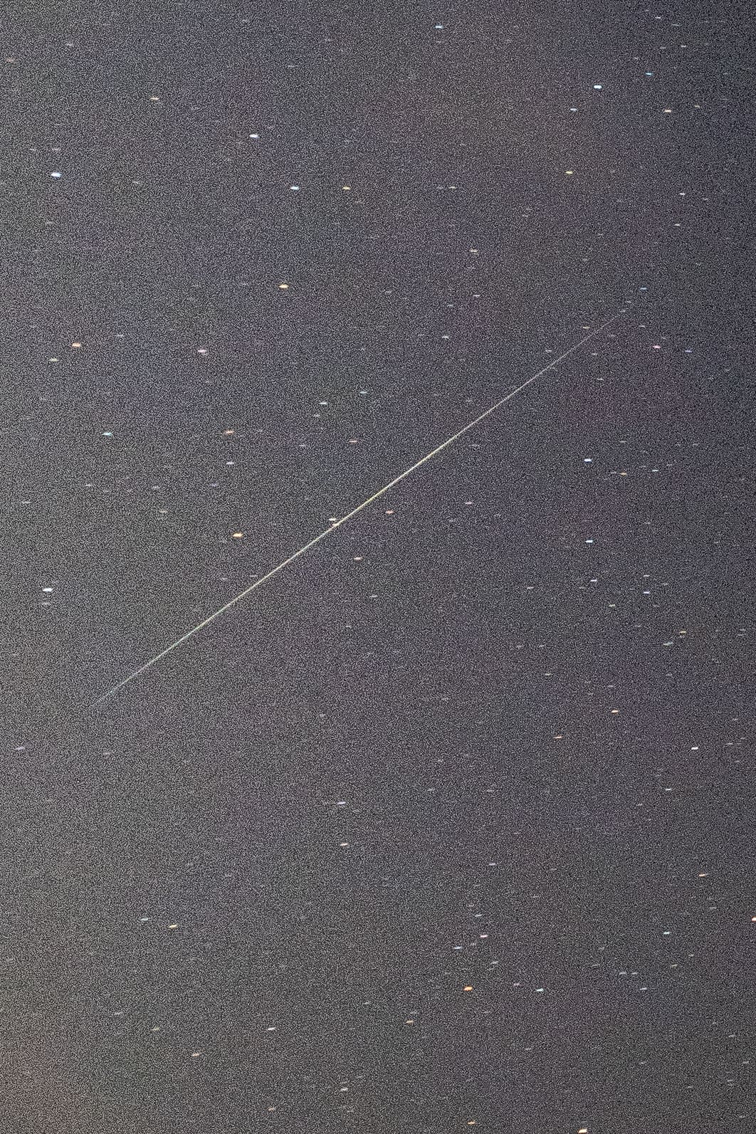 Thin bright meteor streak crossing diagonally through a dense multicolored starfield.