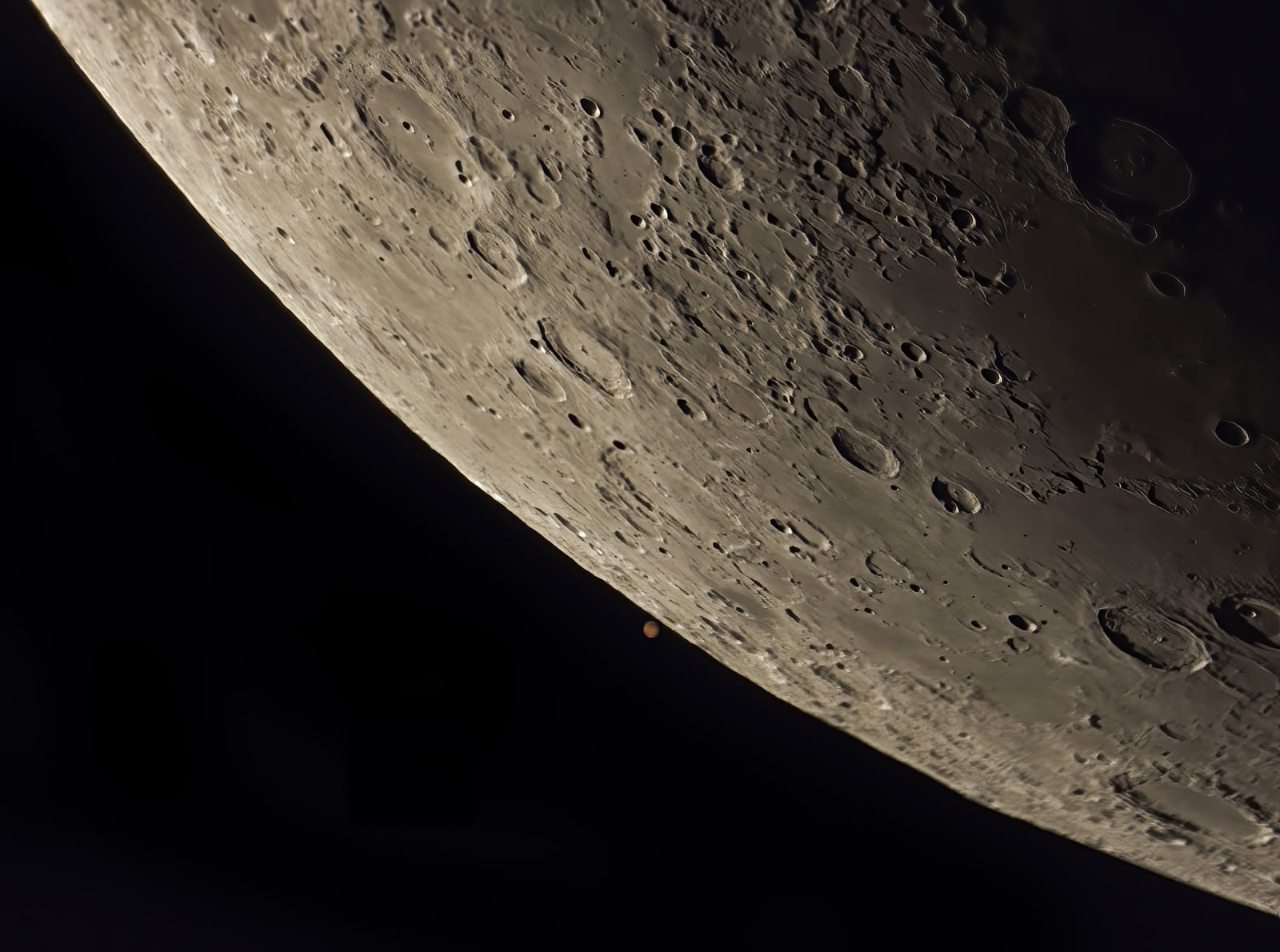 Close telescopic view of the Moon's cratered limb with the small orange disc of Mars visible just beneath it, about to be covered.