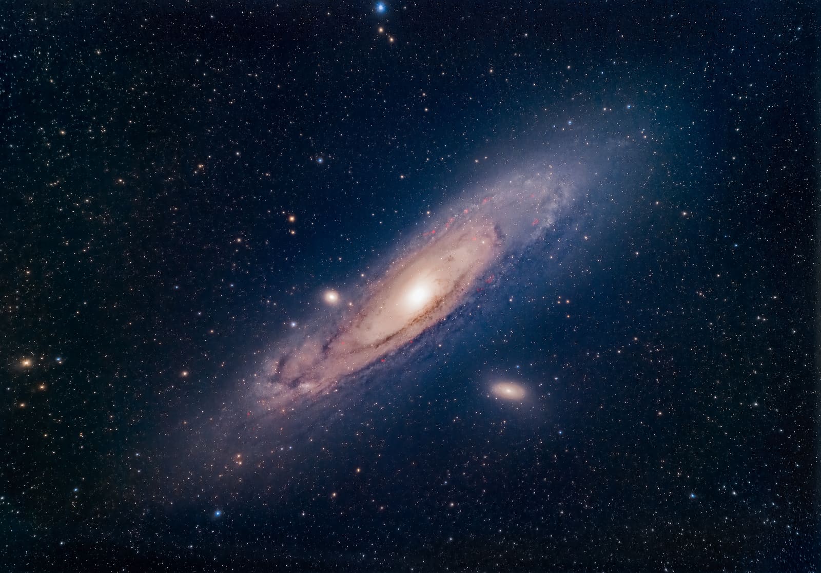 A large tilted spiral galaxy with a bright yellow core and dark dust lanes, surrounded by stars, with two smaller companion galaxies nearby.