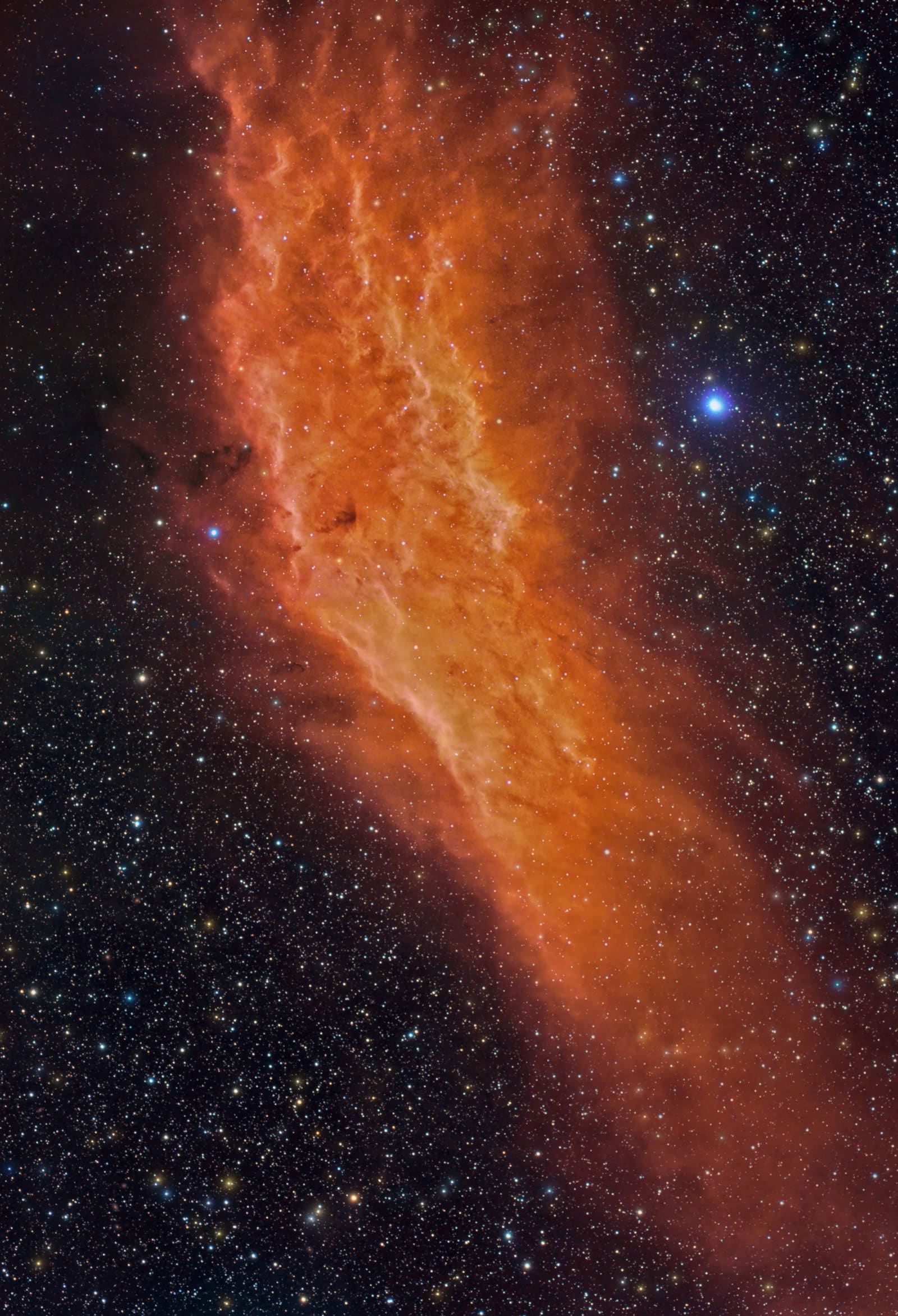 An elongated, flame-like orange nebula stretching diagonally across a starfield, with a bright blue-white star near its base.