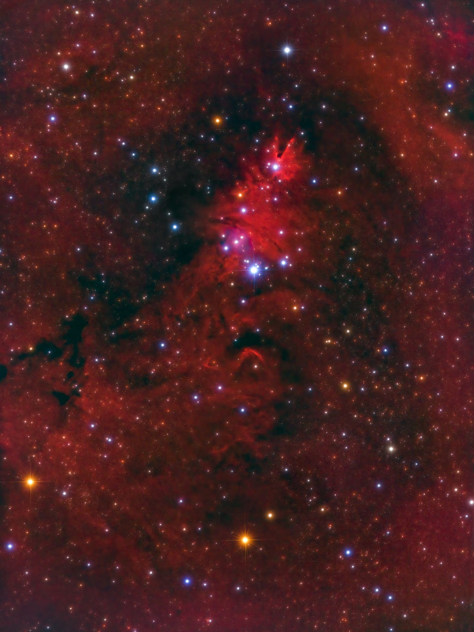 A triangular arrangement of blue stars set against red nebulosity, with a dark conical nebula feature near the top of the frame.