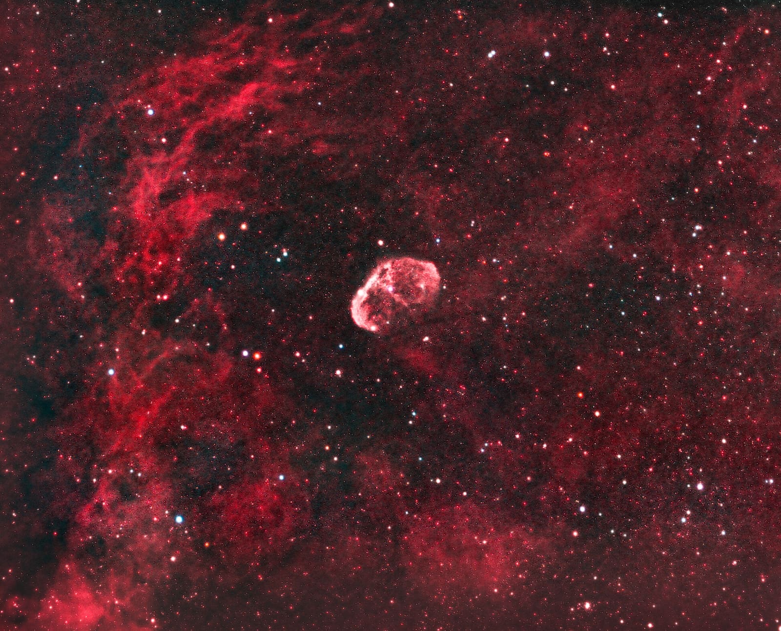 A small round nebula shell centered in a wide field of soft red and pink gas clouds and stars.