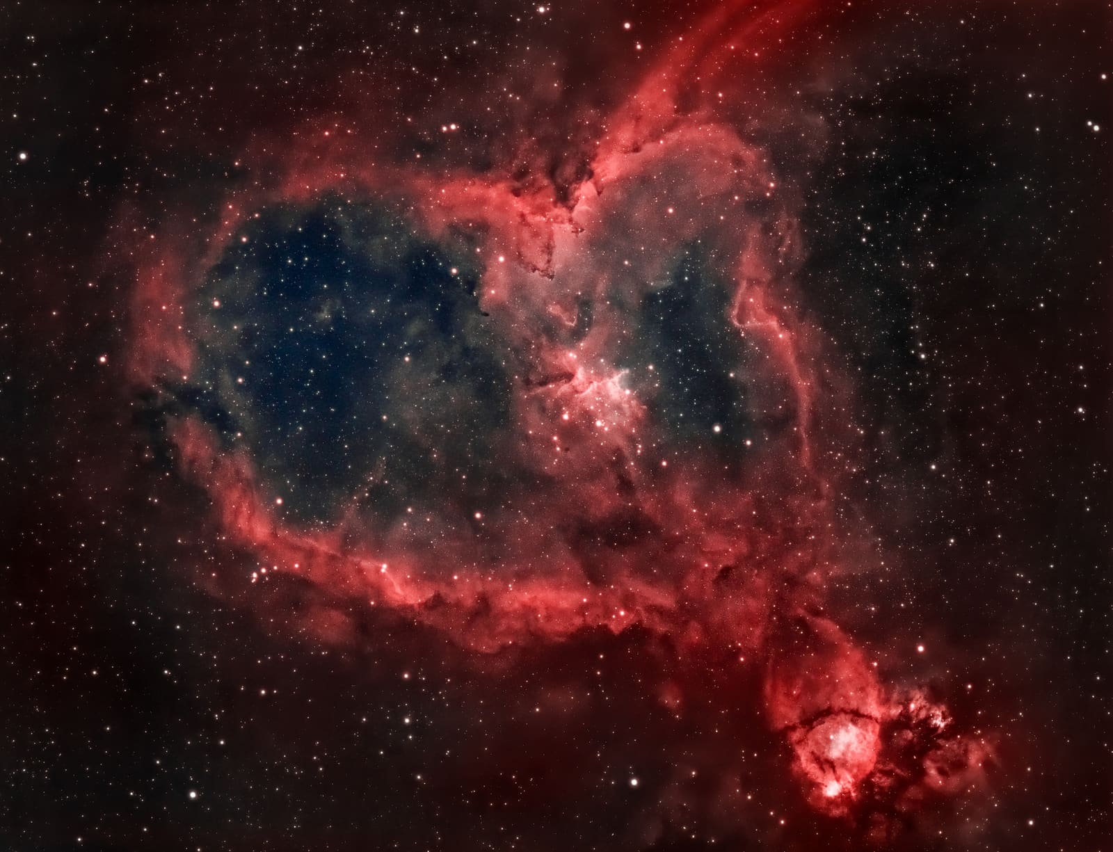 A heart-shaped red nebula with a dark blue-toned interior and a bright star cluster near its center, plus a smaller nebula fragment in the corner.
