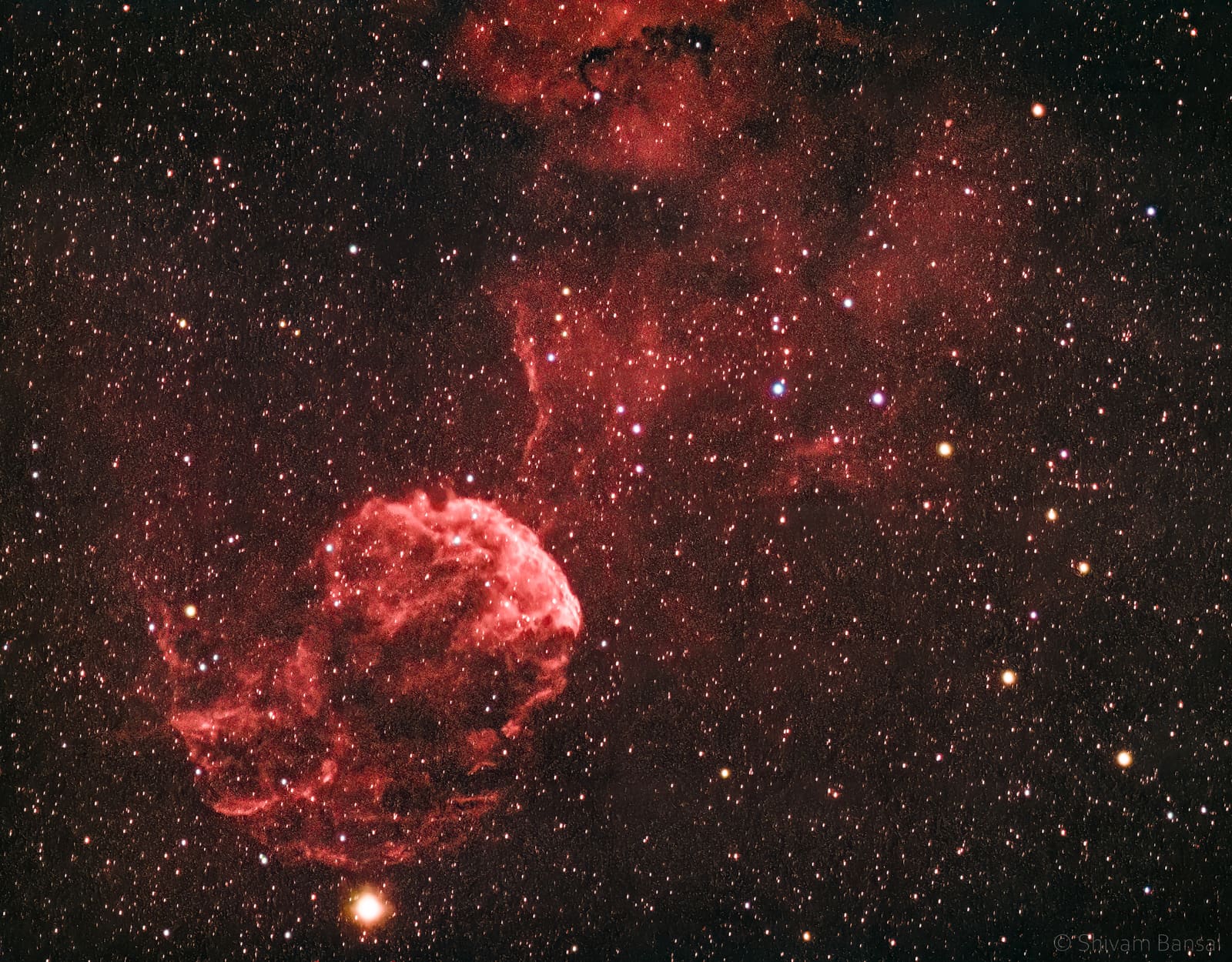 A large, wispy orange-red nebula with tentacle-like filaments spreading across a starfield.