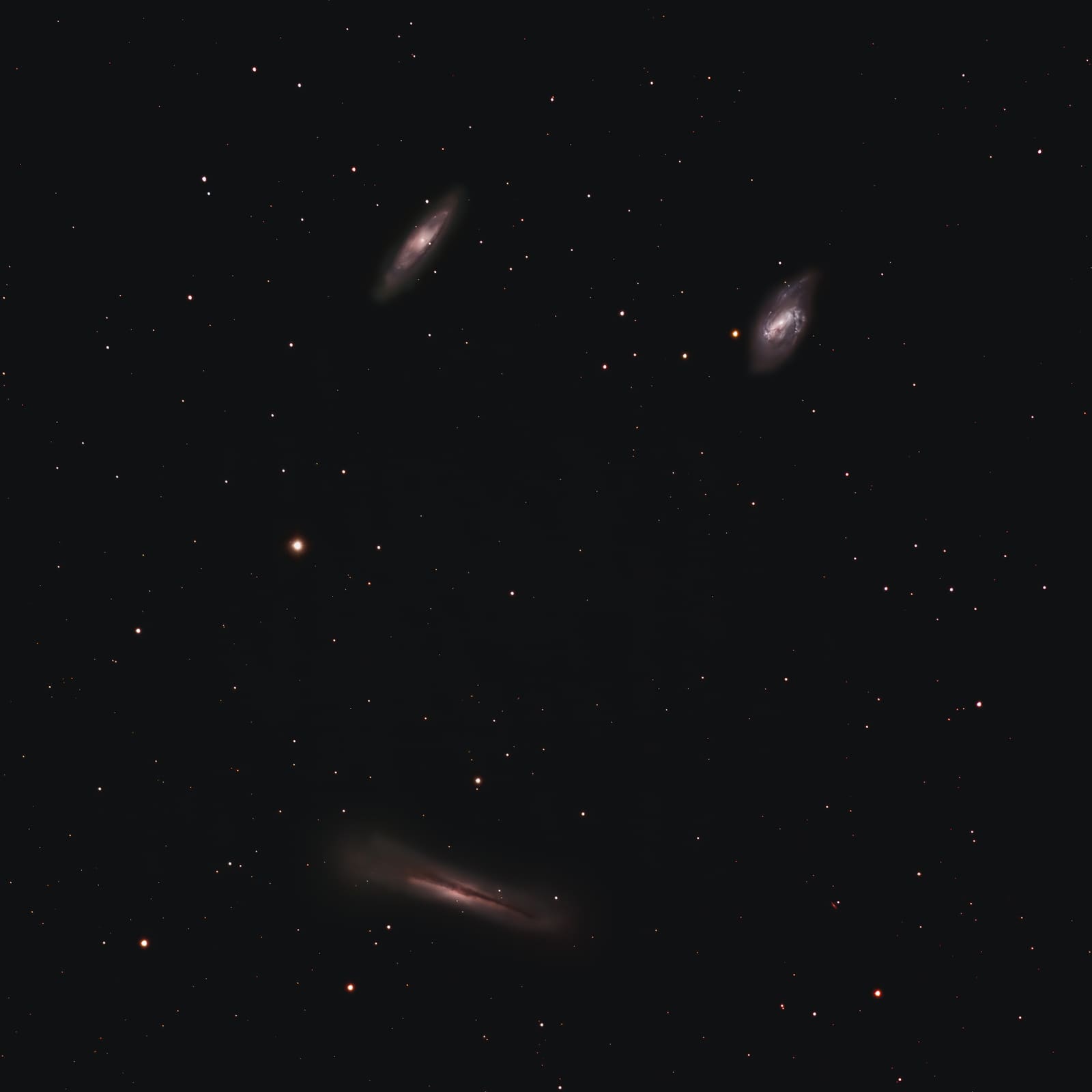 Three faint galaxies scattered across a dark starfield: two oval spirals and one thin edge-on galaxy with a dark dust lane.
