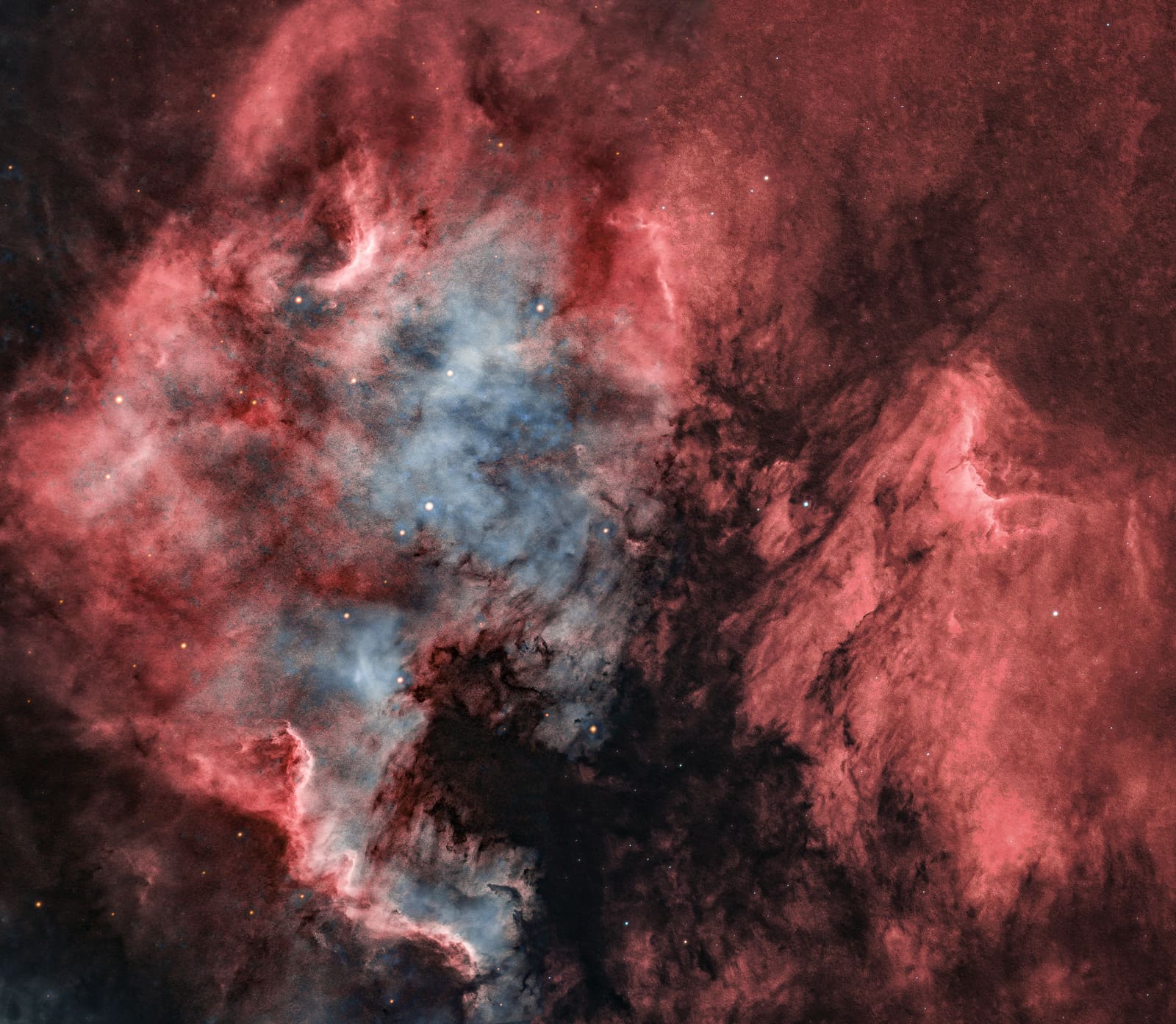 A large red emission nebula shaped like a landmass, with a dark bay-like gap and areas of blue-white nebulosity.