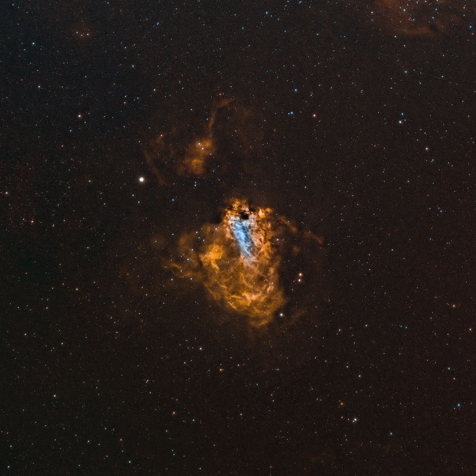 A bright, hook-shaped nebula with orange and blue-white glowing regions surrounded by dark gas.