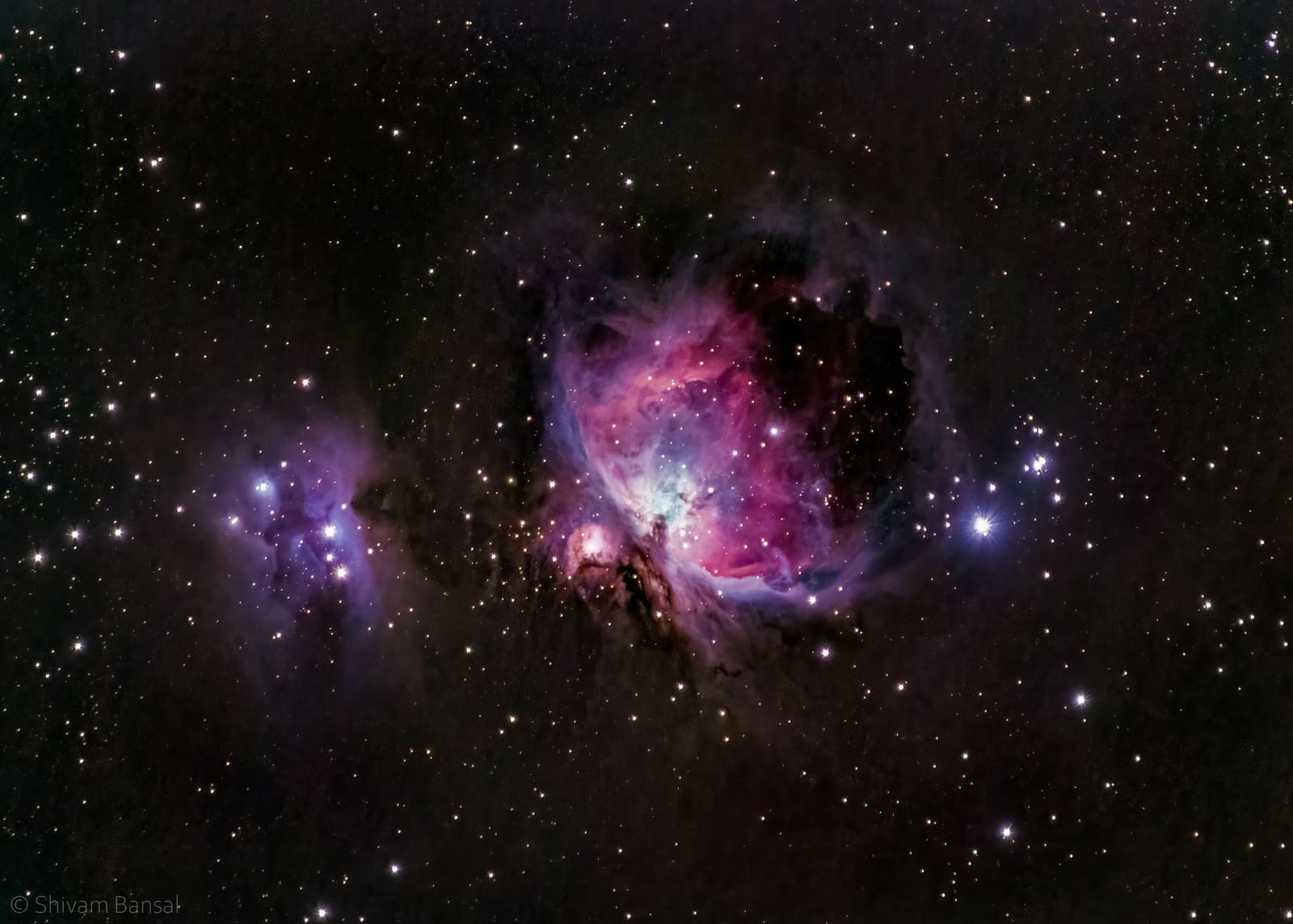 A large bright pink and purple nebula with a glowing white core, alongside a smaller blue nebula to the left.