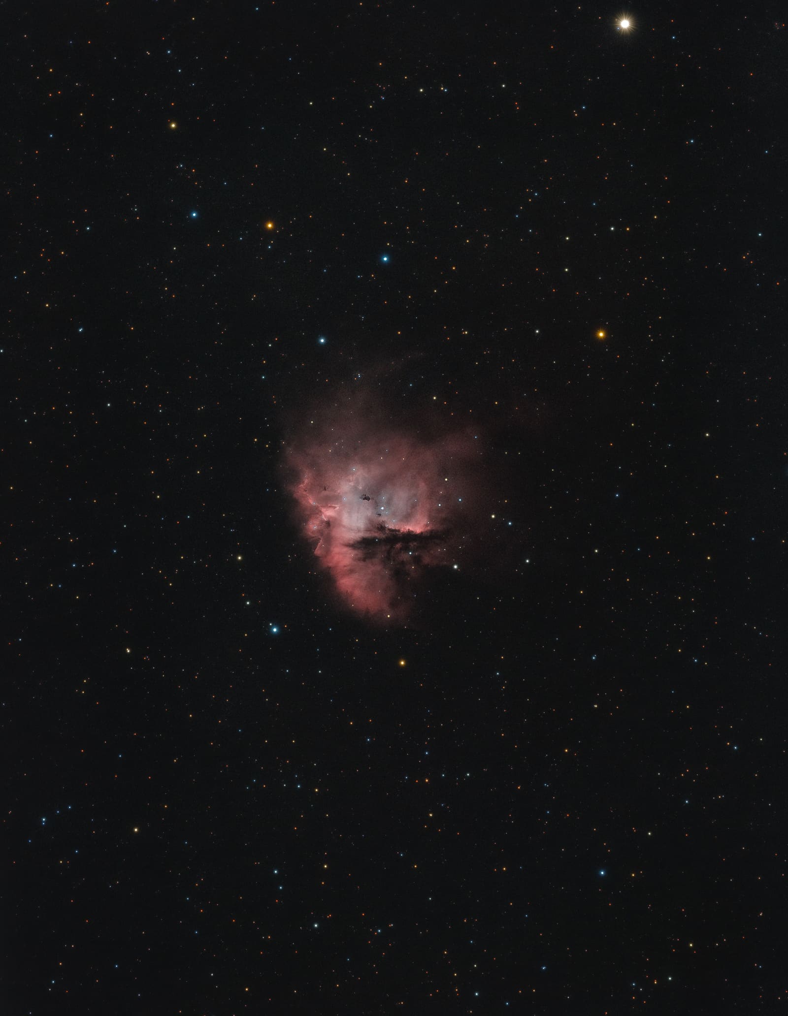 A rounded pink and red nebula with a dark wedge-shaped gap, resembling the video game character Pac-Man.