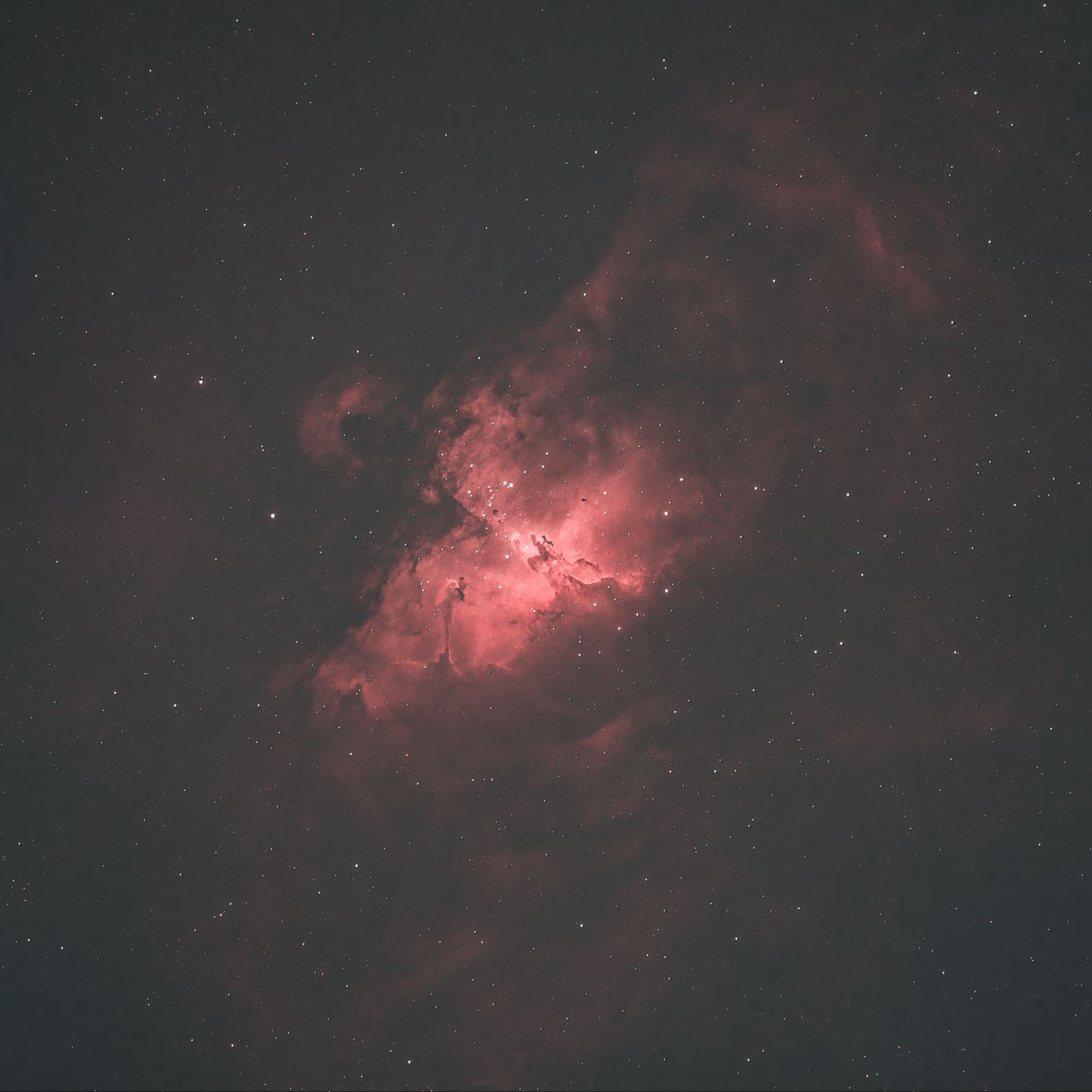 Three dark, finger-like pillar structures rising from bright red and pink nebulosity, with scattered stars around.