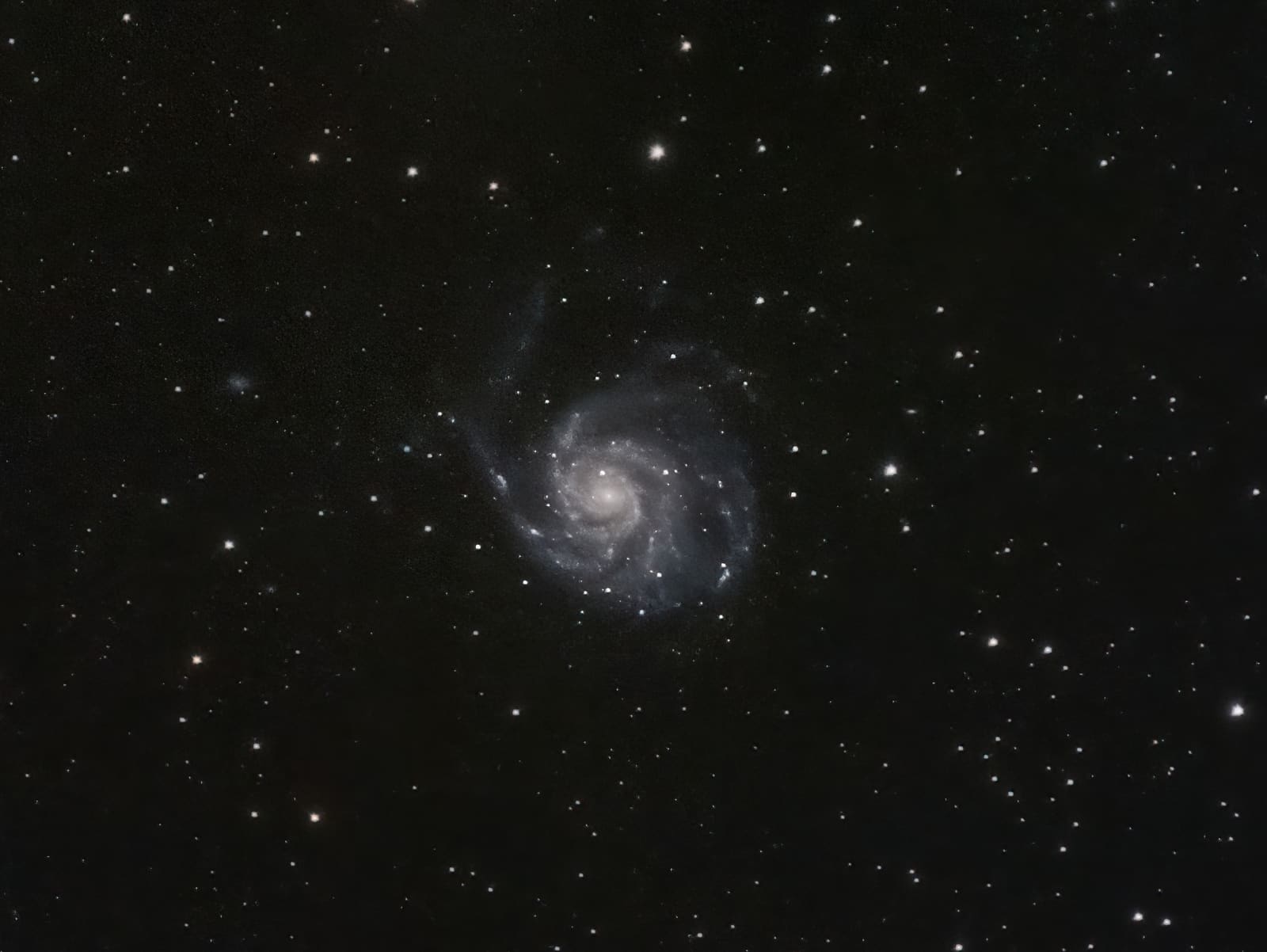 A faint, loosely wound spiral galaxy with a bright core, set against a dark starfield with a small companion galaxy nearby.