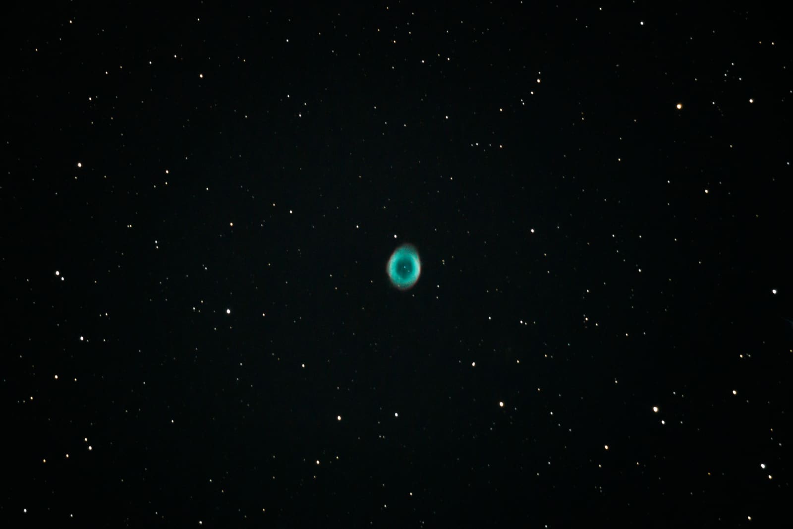 A small, distinct teal-blue ring-shaped nebula centered in an otherwise dark, sparsely starred frame.