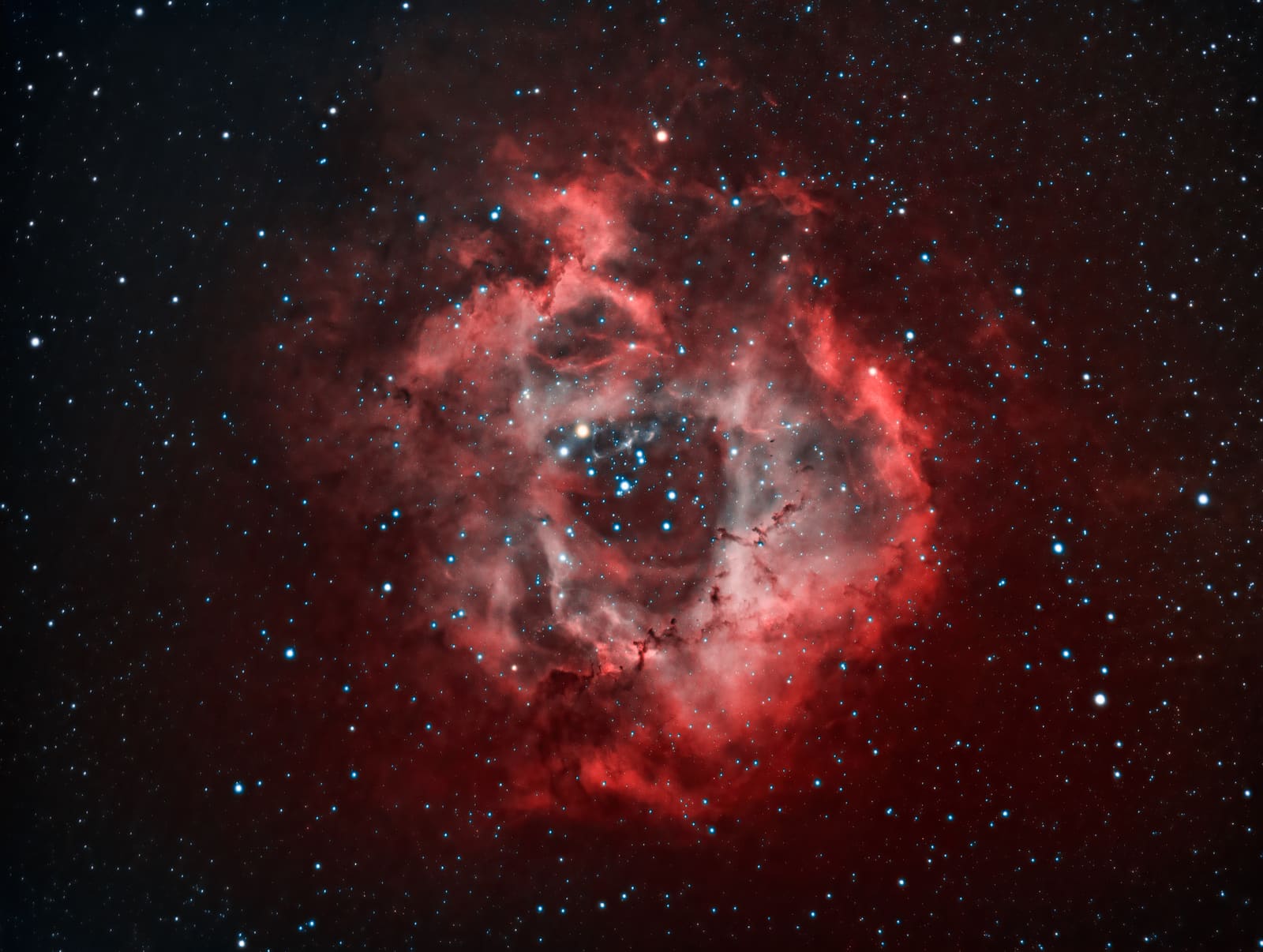 A large red ring-shaped nebula with a dark central cavity containing a cluster of bright stars.