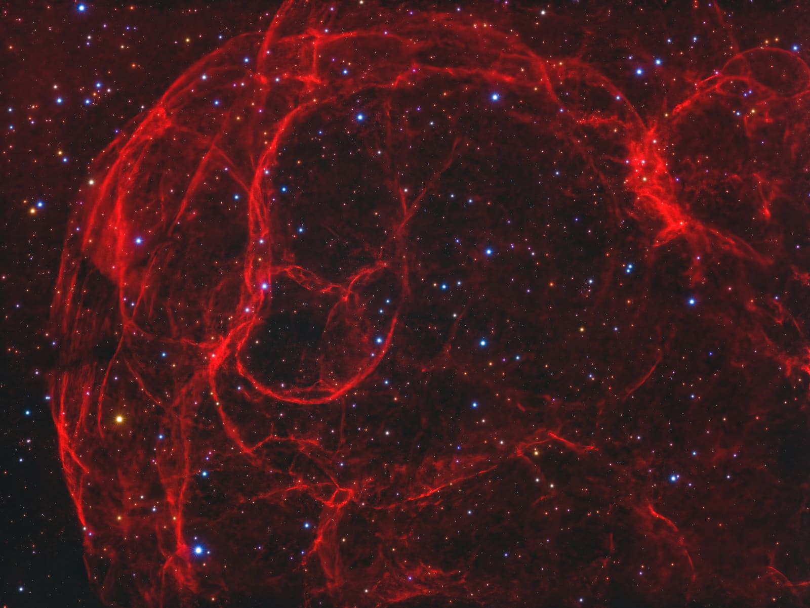 A wide network of thin, looping red filaments spread across a starfield, resembling tangled strands.