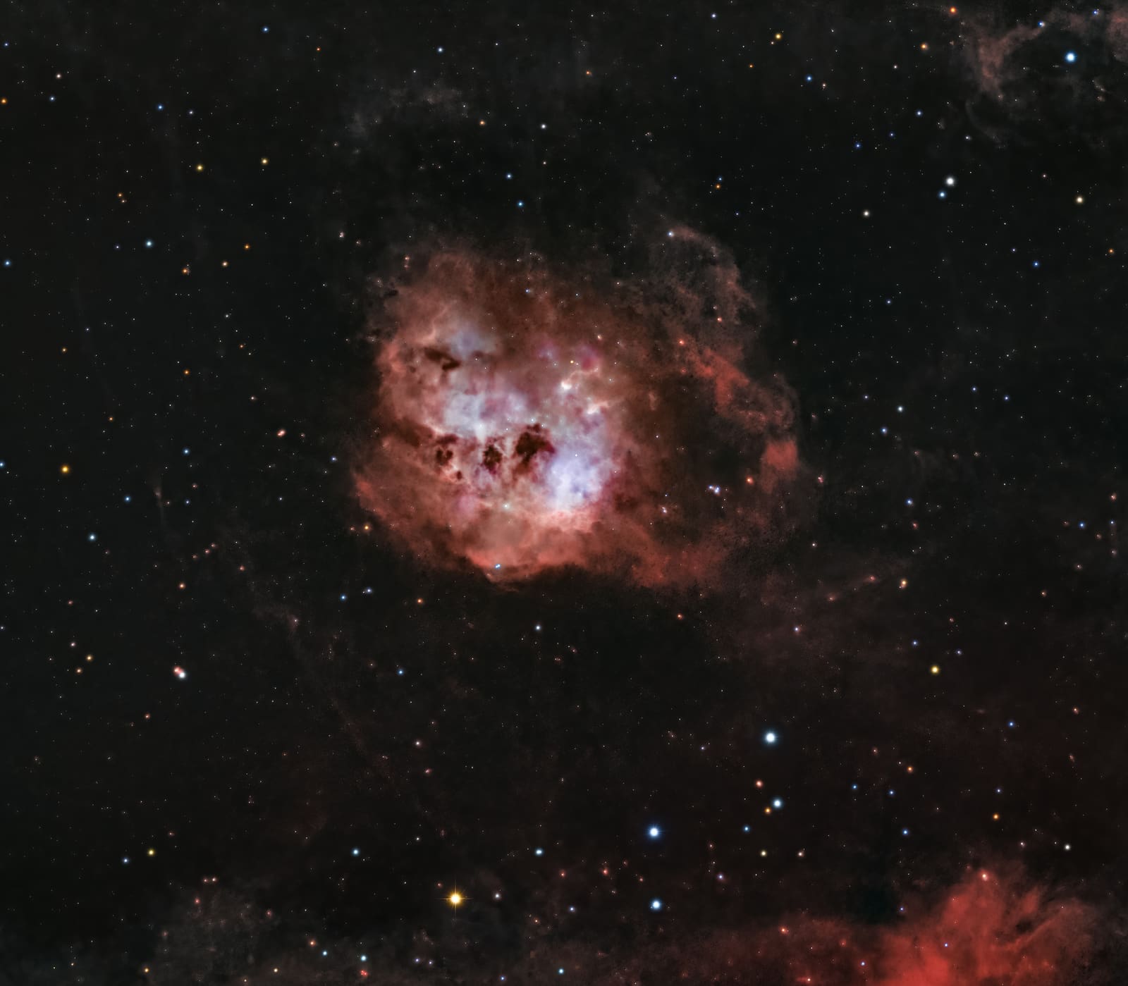 A roughly circular glowing nebula with a bright white-orange center and dark patches, surrounded by a soft red halo.