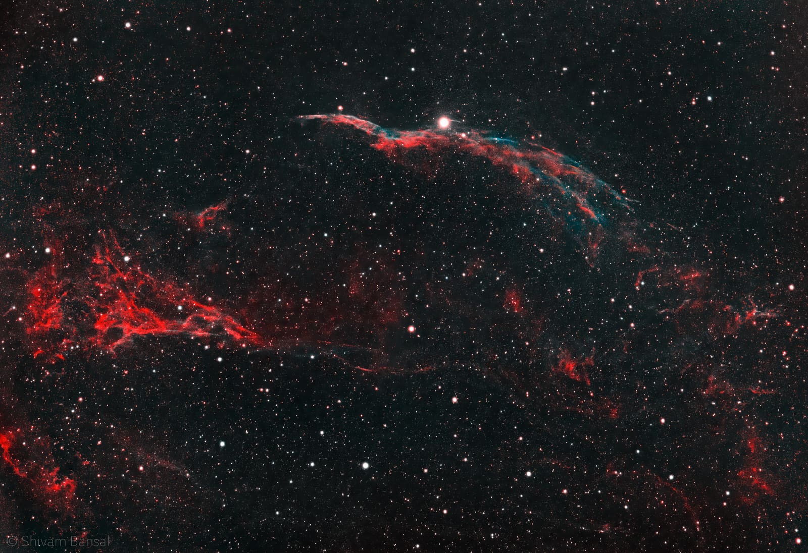 A curved, wispy red and teal filament arcing across a starfield, with a bright star along its edge and a fainter straight filament crossing below.