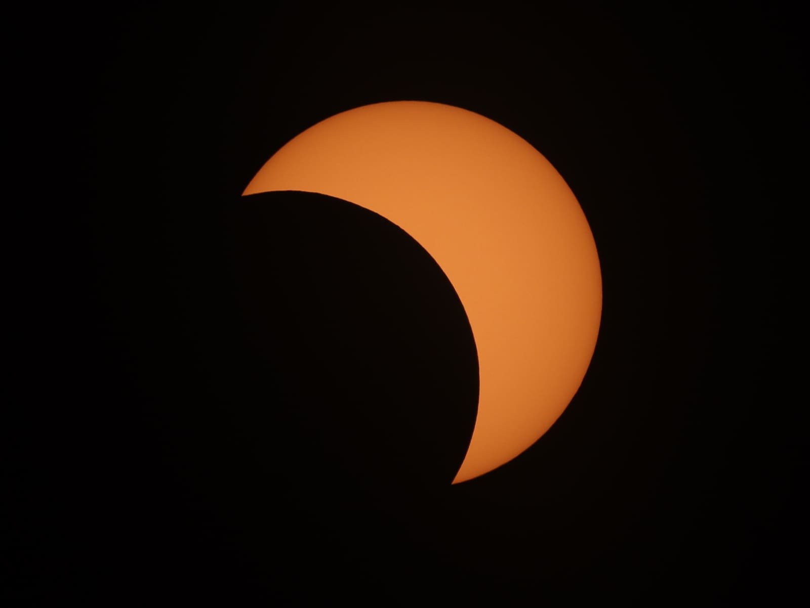 A thin orange crescent of the Sun against a black sky, most of the solar disc covered by the Moon.