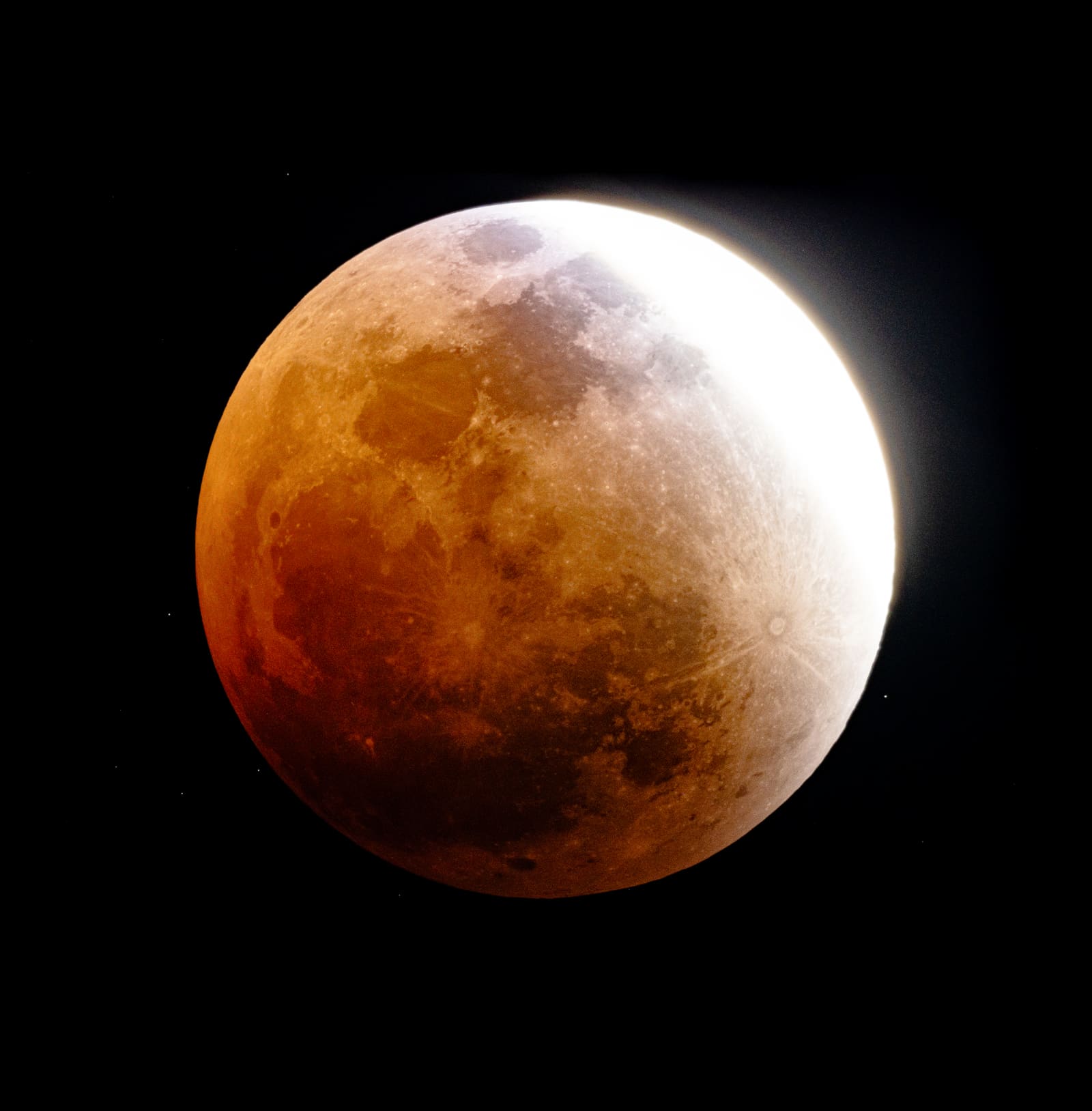 A deep red totally eclipsed moon with one bright white sliver of light along its edge, surface detail visible across the red disc.