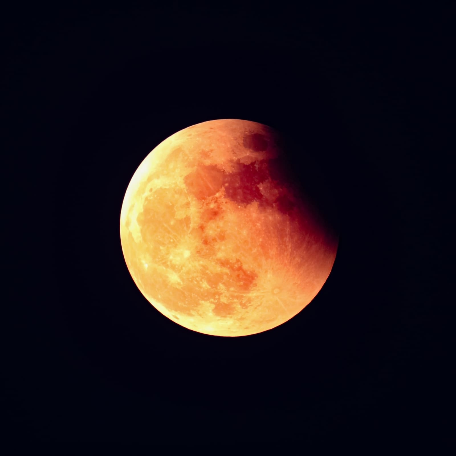 A moon glowing deep orange-red over most of its surface, with a small brighter crescent still visible on one edge, set against a dark sky.