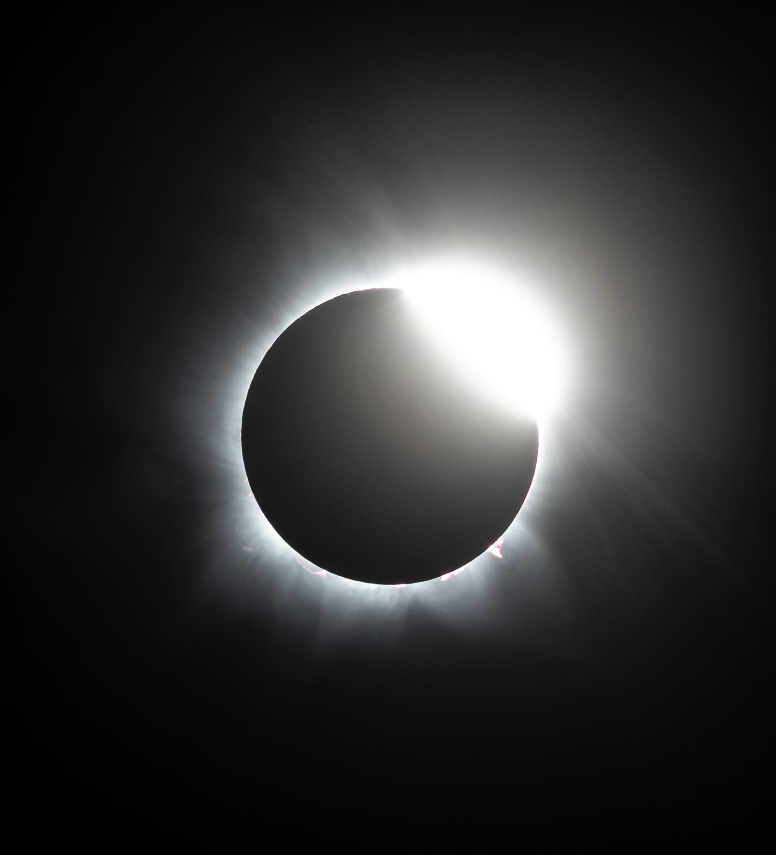 A dark eclipsed sun with one bright point of light on its edge and a faint ring of corona around it, forming a diamond-ring shape.