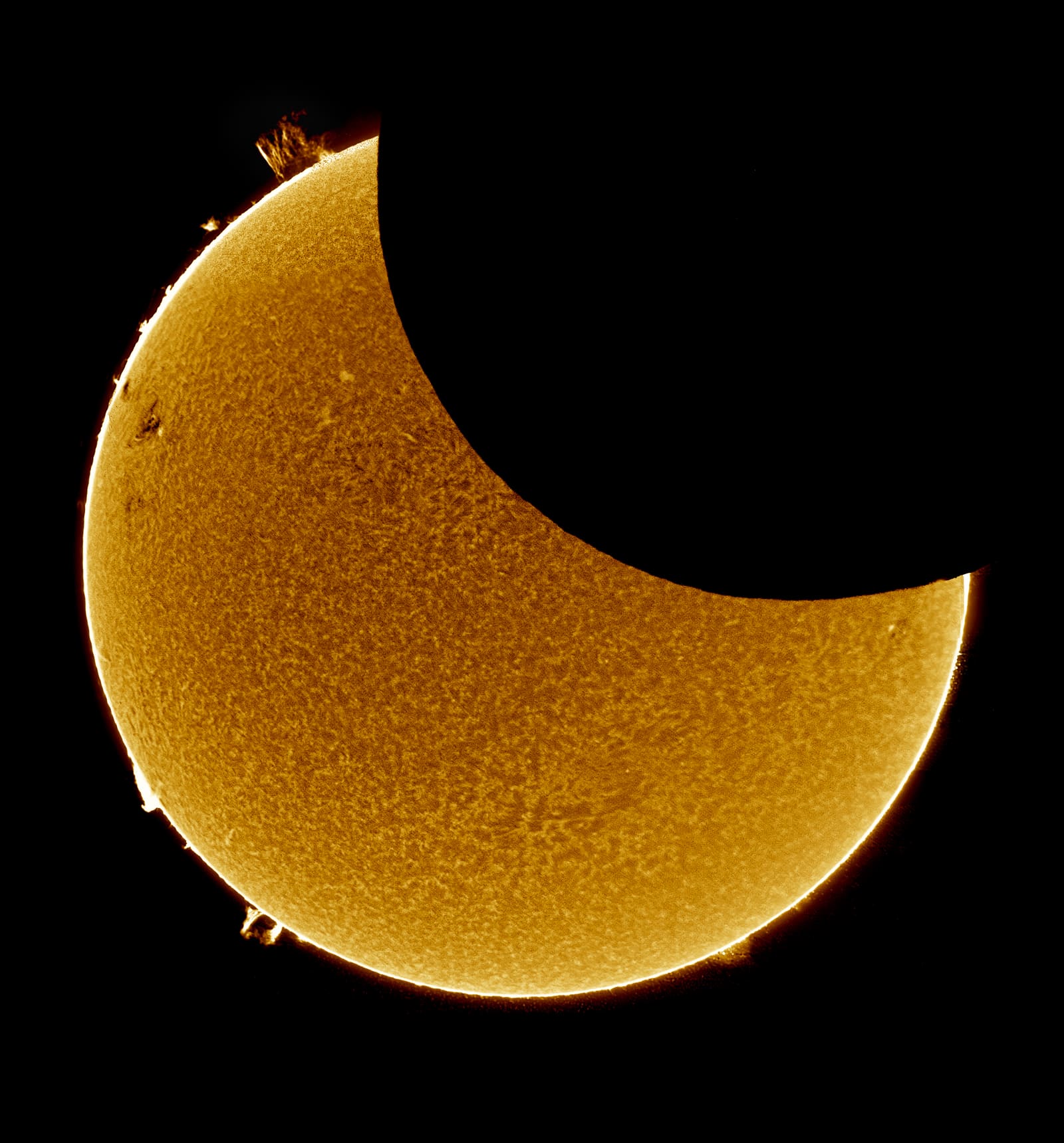 A partially eclipsed orange sun with a dark bite taken from its lower edge and several small dark sunspots visible on its surface.