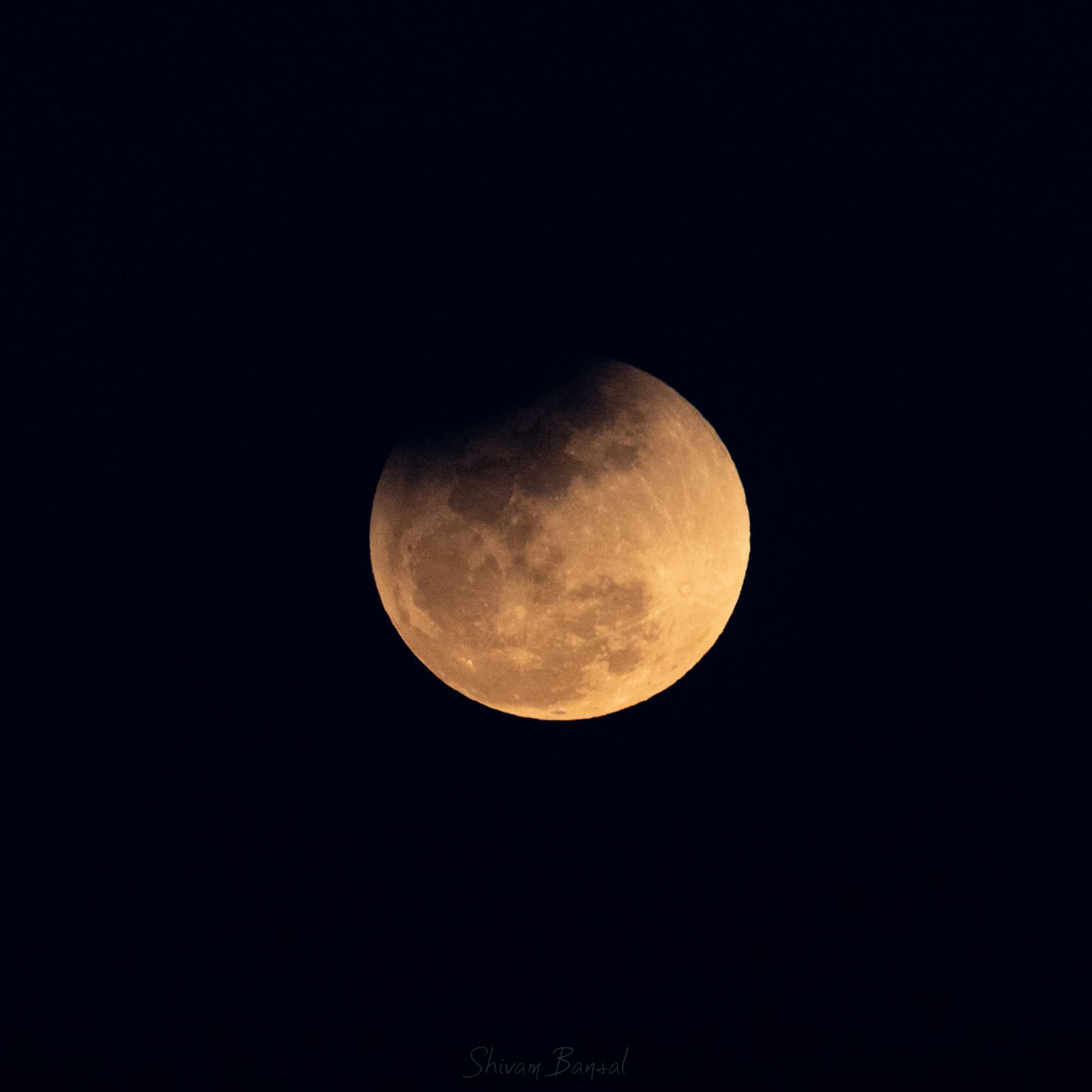 A gibbous-looking moon with roughly half its disc darkened to a dull orange-brown by Earth's shadow, the rest still bright.