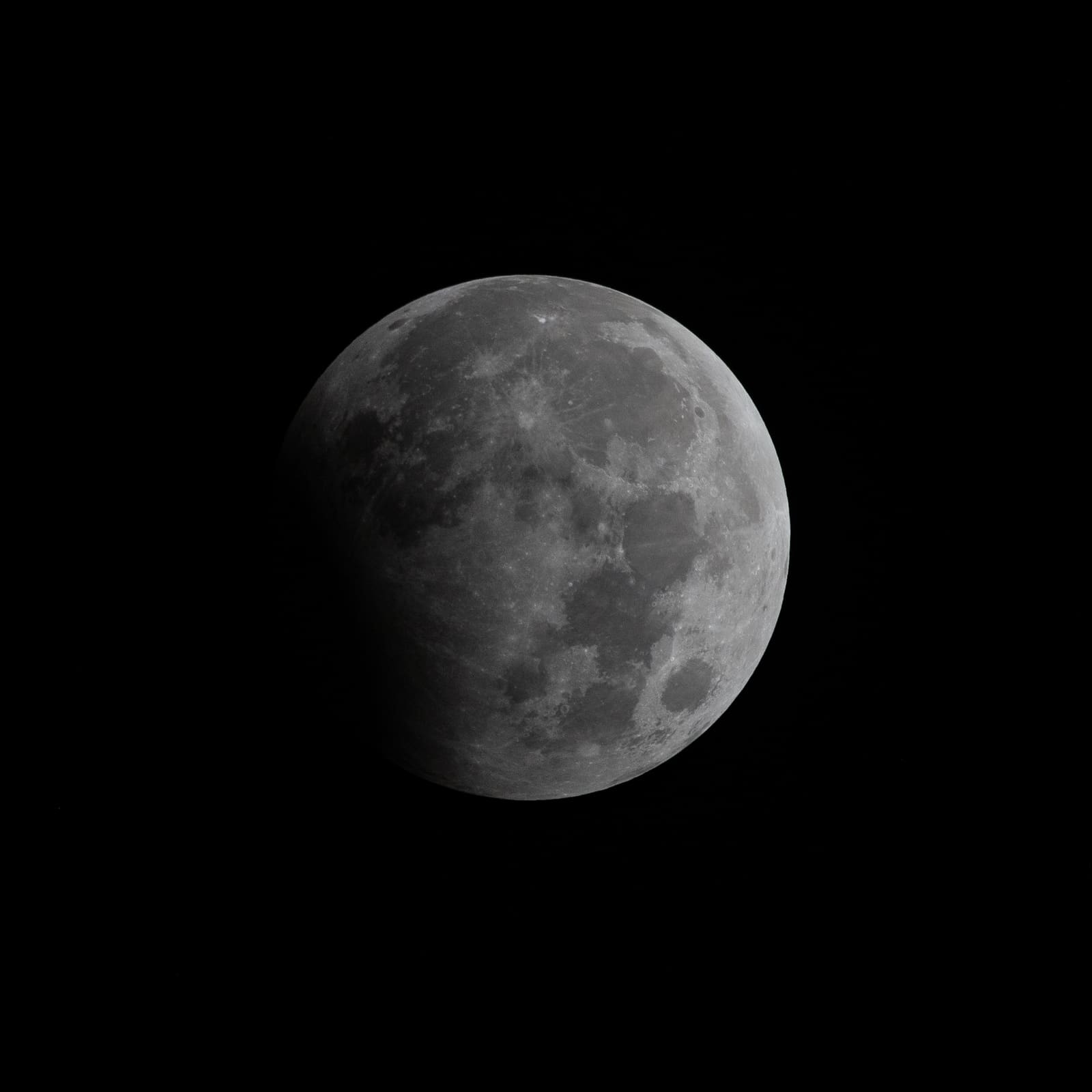 A full moon with a dark shadow covering a small portion of its upper edge.