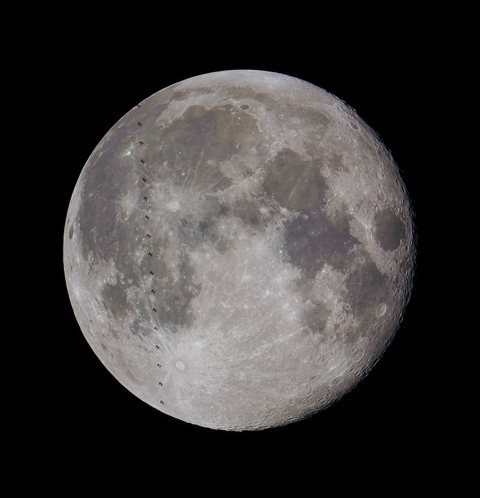 Full Moon showing detailed craters and maria, with a diagonal line of small dark silhouette dots marking the ISS's transit path across it.