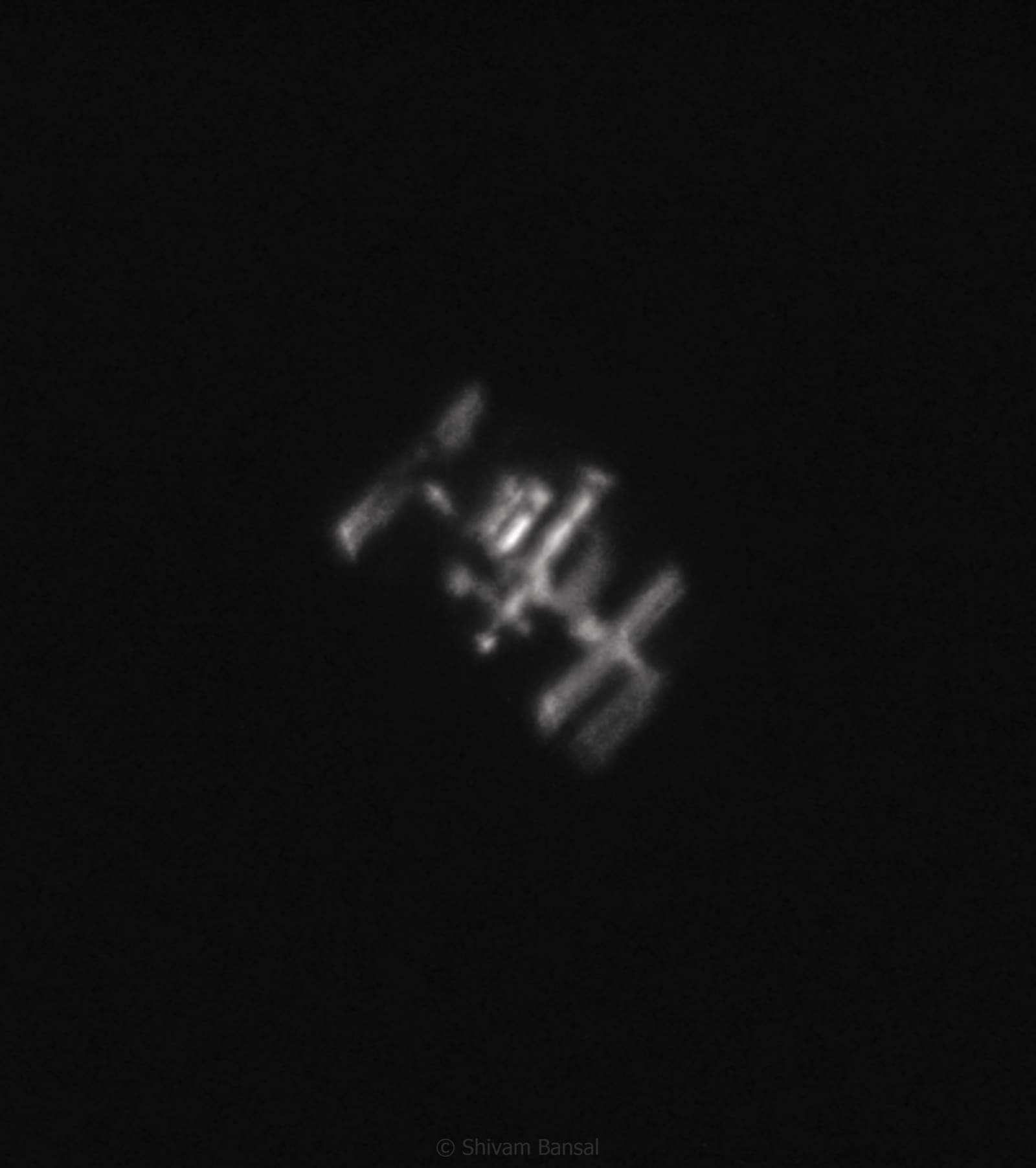 Grainy but detailed telescopic photo of the International Space Station showing its solar panels and module trusses in silhouette and light.