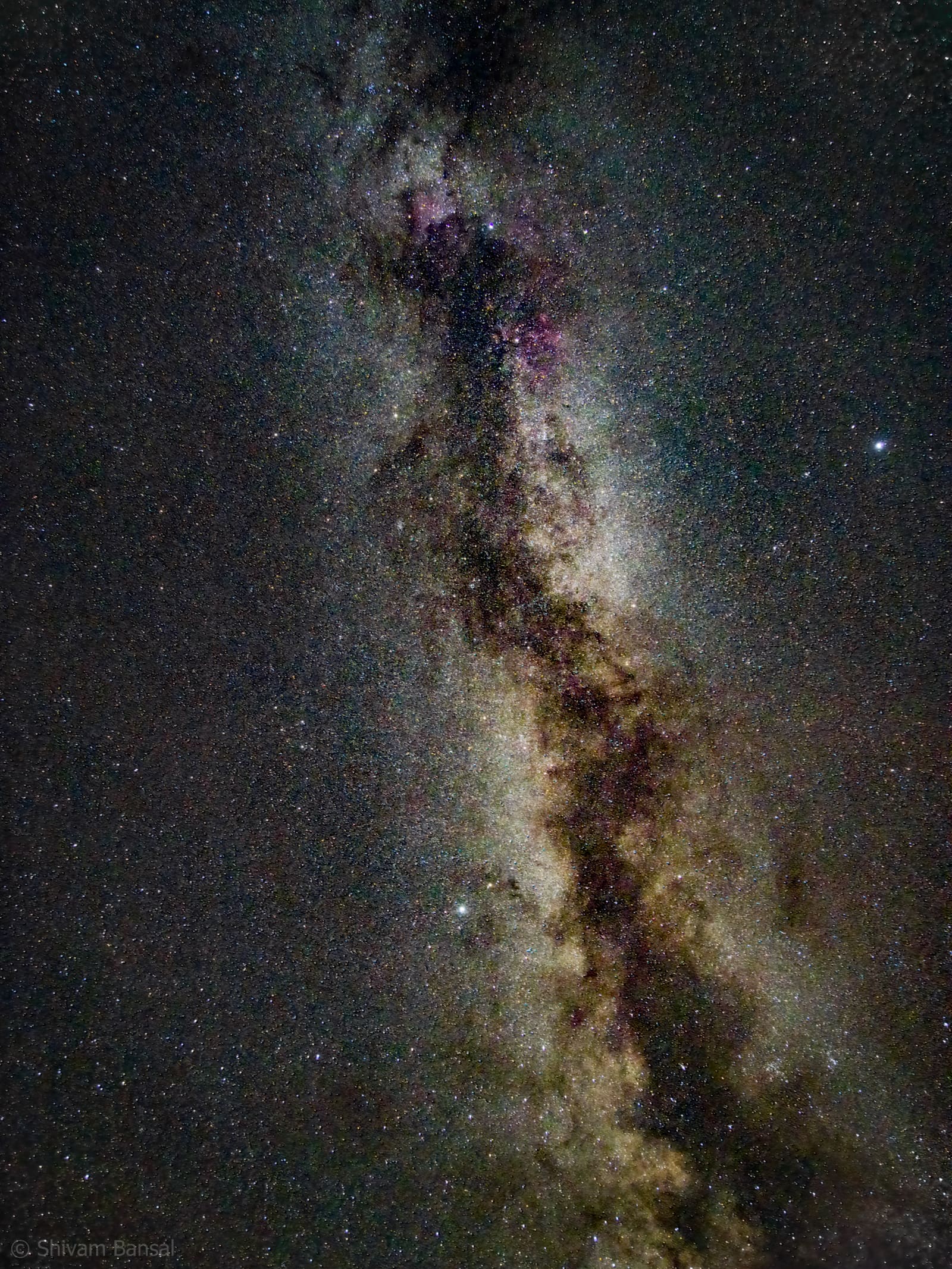 Wide vertical shot of the Milky Way core directly overhead near Bera, Rajasthan, showing golden star clouds and faint magenta nebulosity.