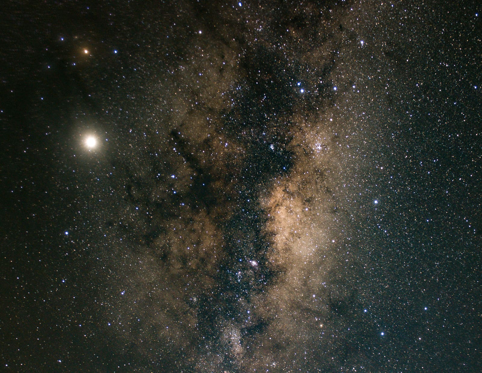 The Milky Way core beside a bright planet, showing detailed dust lanes and star clouds against a dark sky.