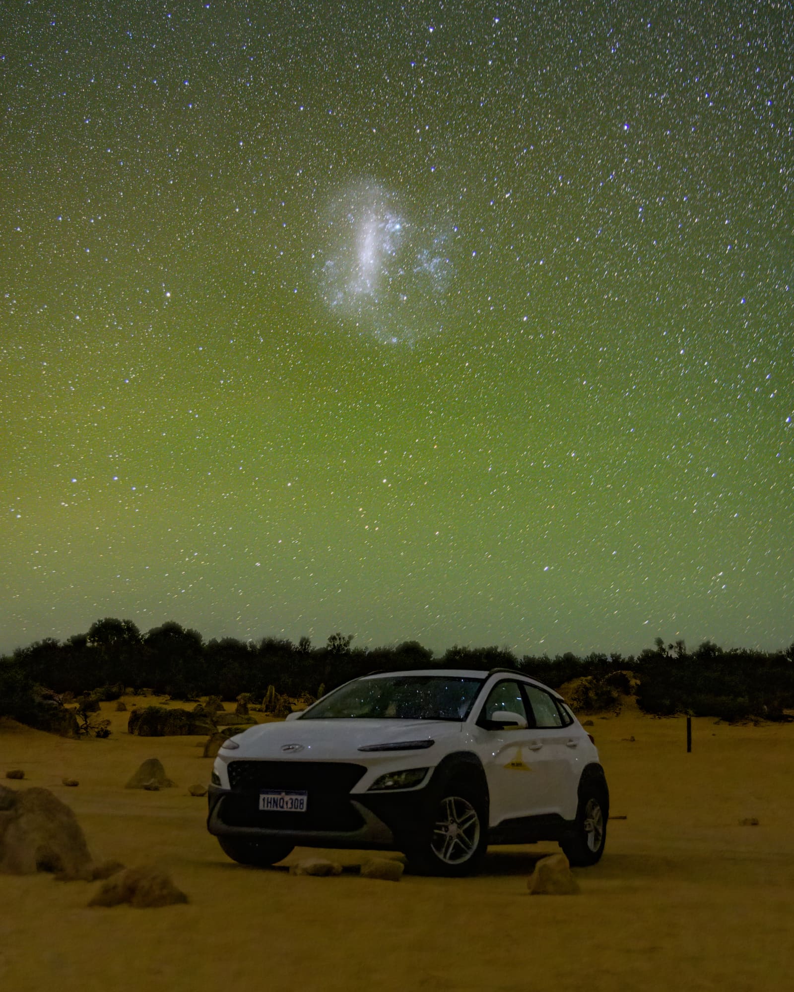 A parked car under a green night sky in the Australian outback, with the Large Magellanic Cloud visible above.