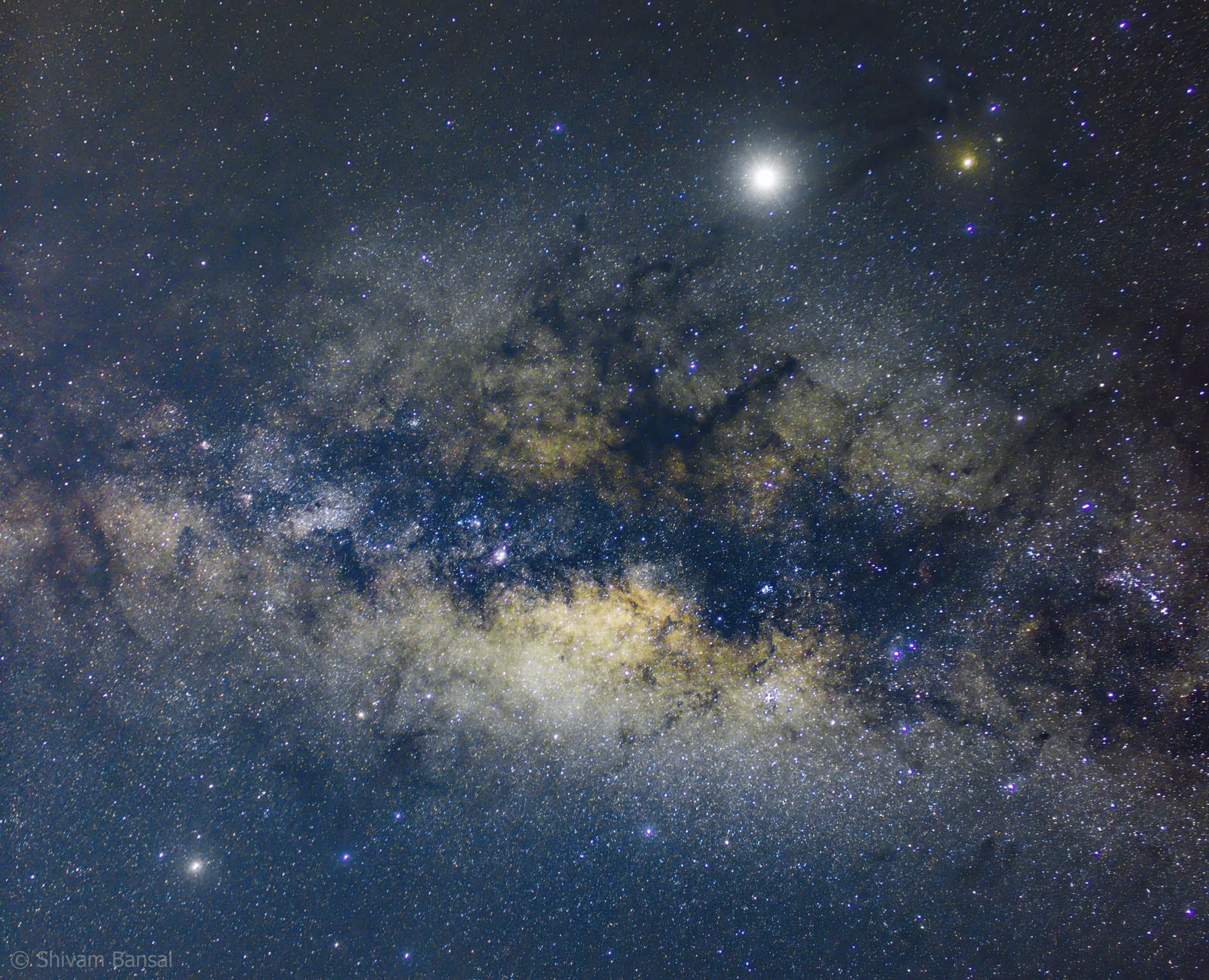 Close-up view of the Milky Way core region near Sagittarius, showing dense star clouds and dark dust lanes against a blue night sky.