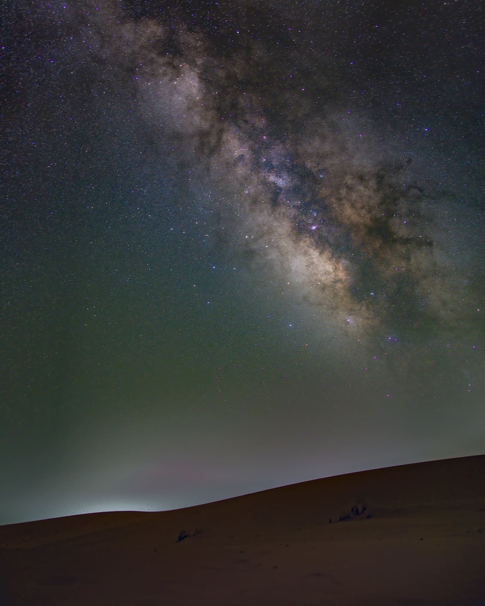 The bright Milky Way core over rippled sand dunes in the Sahara Desert at night.