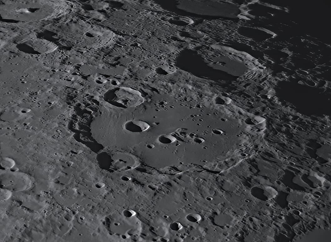 A large lunar crater with a curved chain of smaller craters arcing across its floor.
