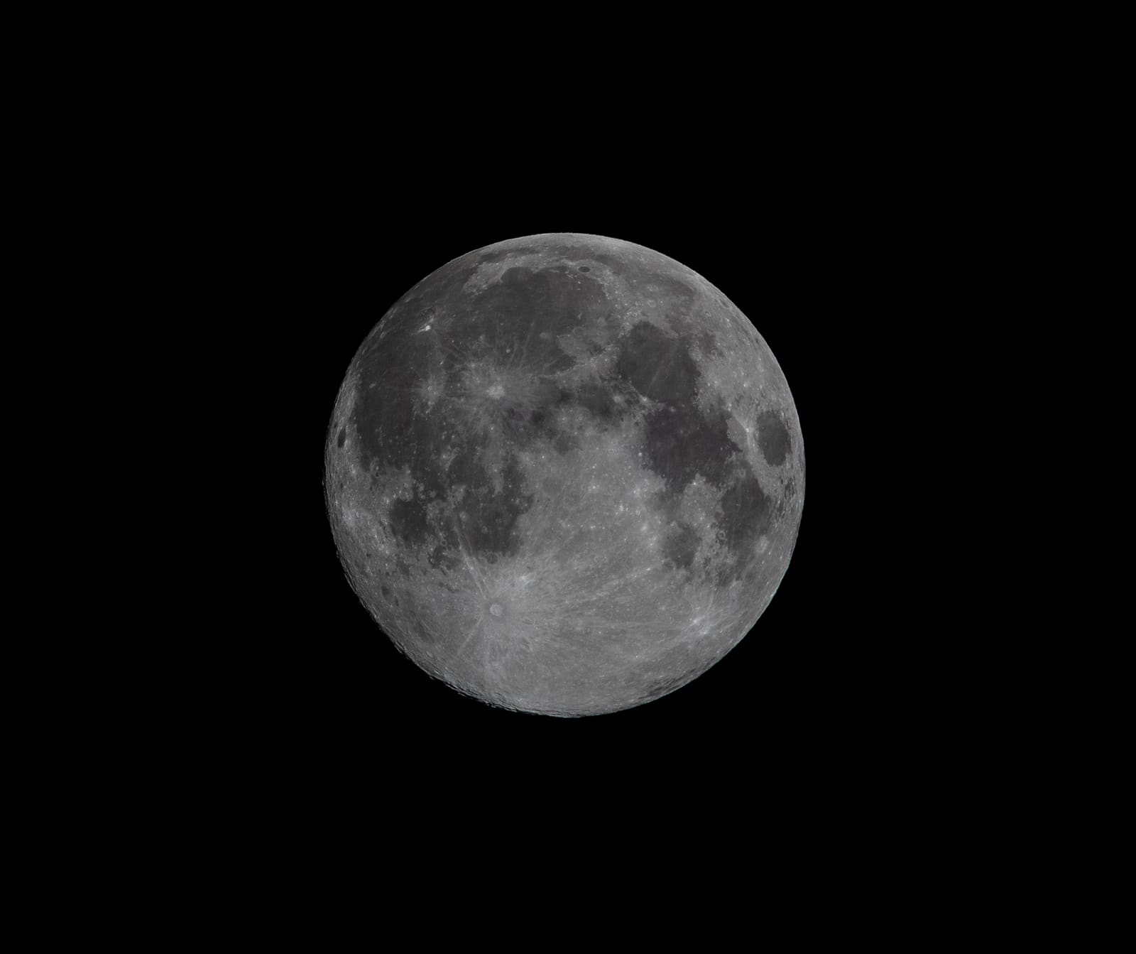 A nearly full moon showing faint grey mare patches and bright ray craters across an evenly lit disc.