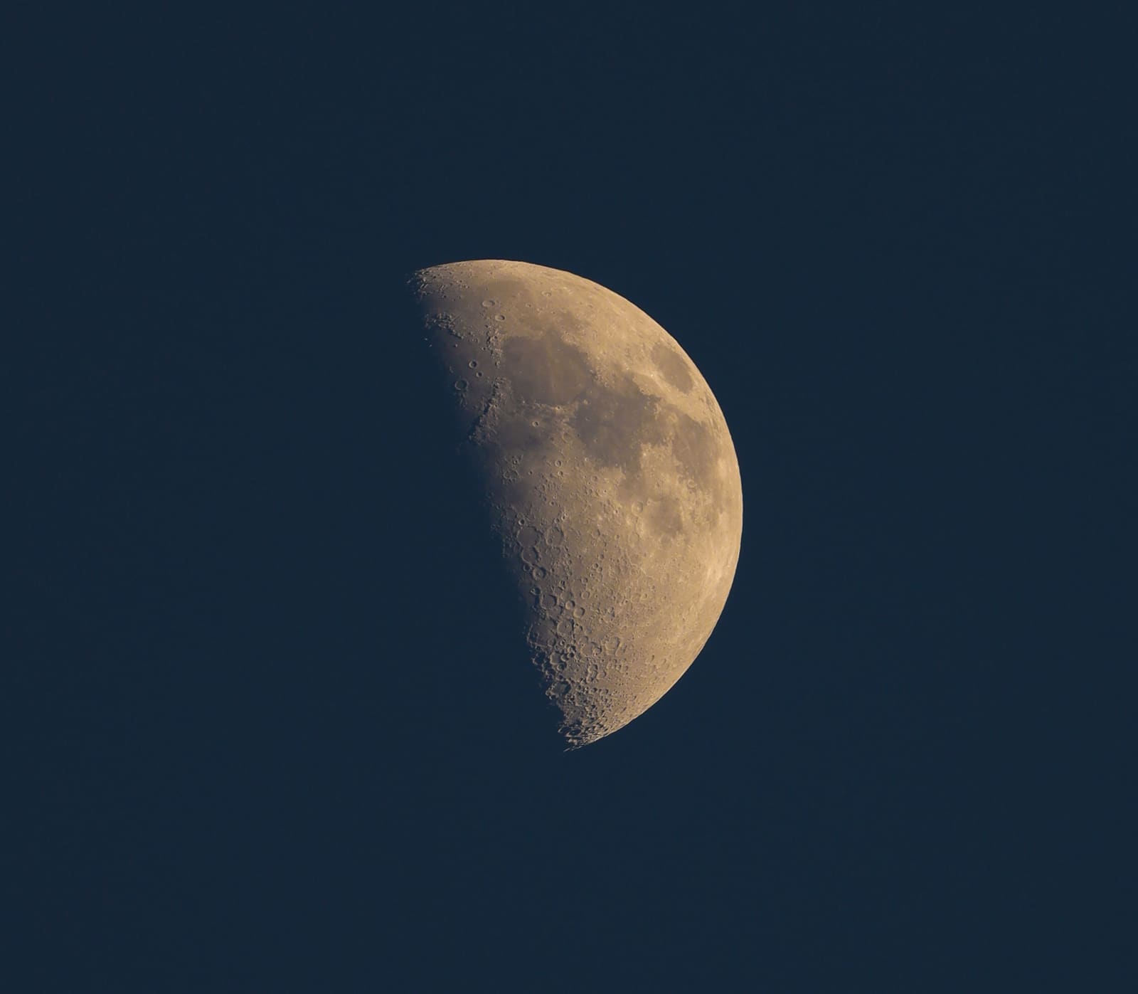 A half-illuminated moon with a sharp straight terminator line dividing bright and dark halves, craters visible near the edge.
