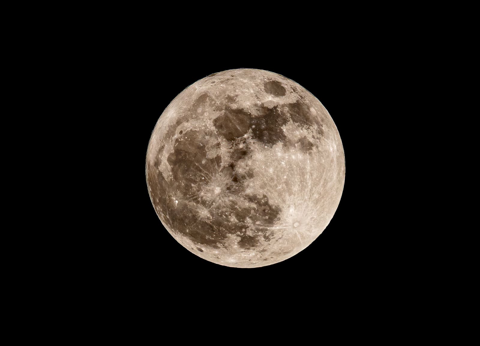 A full moon glowing orange low in the sky, partly veiled by clouds, with dark tree branches silhouetted in the foreground.