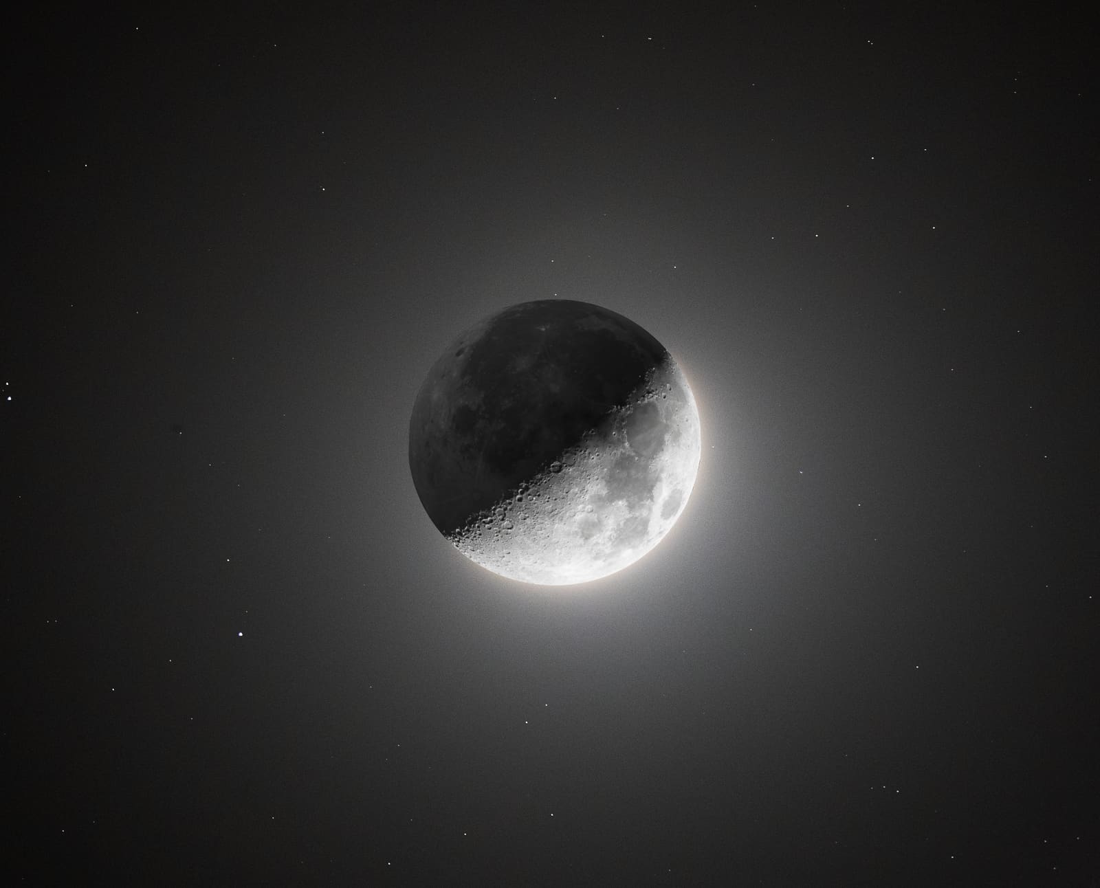 A crescent moon photographed with HDR processing so the dark side is also faintly visible, glowing softly against a black sky.