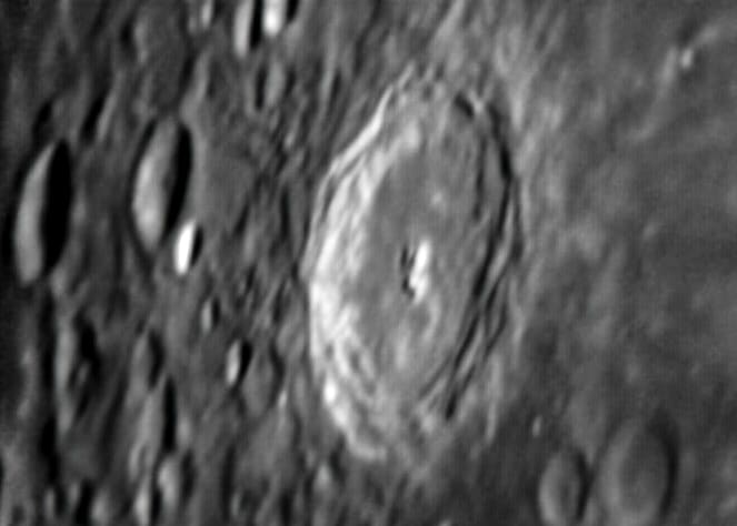 An oblique view of a large crater near the curved edge of the Moon, appearing oval due to the viewing angle.