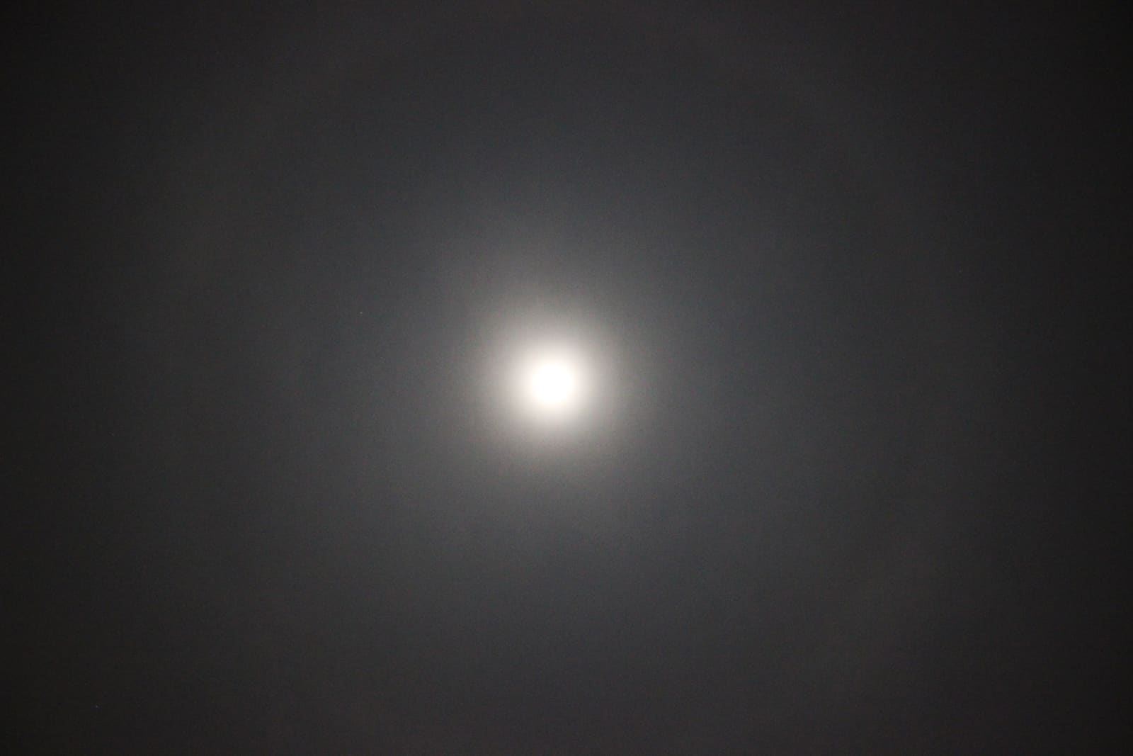 A full moon surrounded by a large faint circular halo of light against a dark sky.