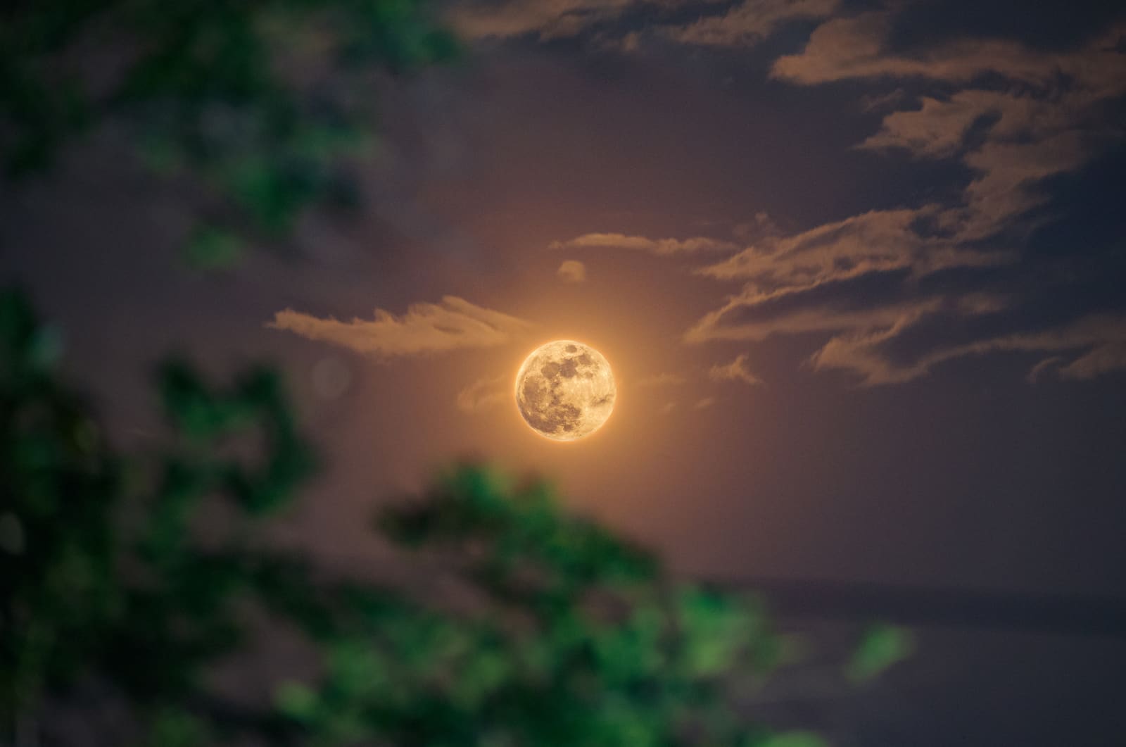 A warm amber-toned full moon with visible mare and crater detail against a black background.