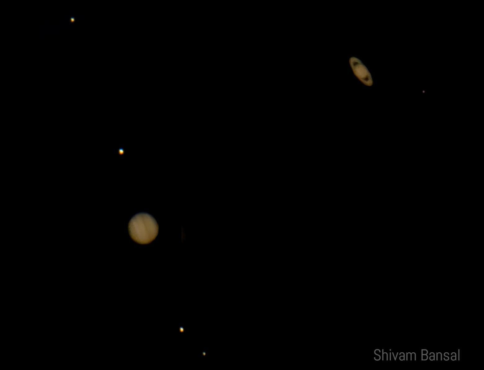 Telescopic image showing Jupiter with its four Galilean moons in a line and Saturn with its rings visible in the same wide field of view against black space.