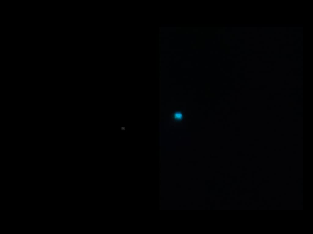 Telescopic image of Neptune as a very small teal-blue disc with its moon Triton visible as a faint point of light nearby, against black space.