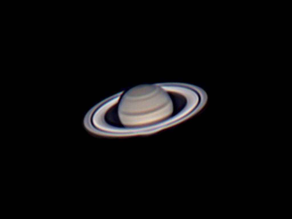 Telescopic image of Saturn with its rings tilted toward the viewer, showing the dark Cassini Division gap and subtle cloud banding on the planet's disc.