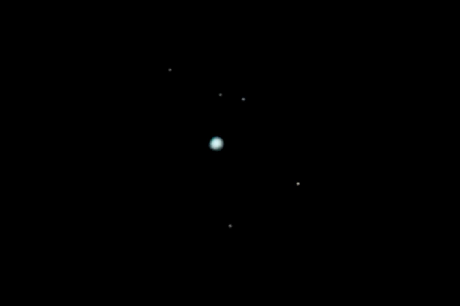 Telescopic image of Uranus as a small pale cyan disc surrounded by several faint point-like moons against black space.