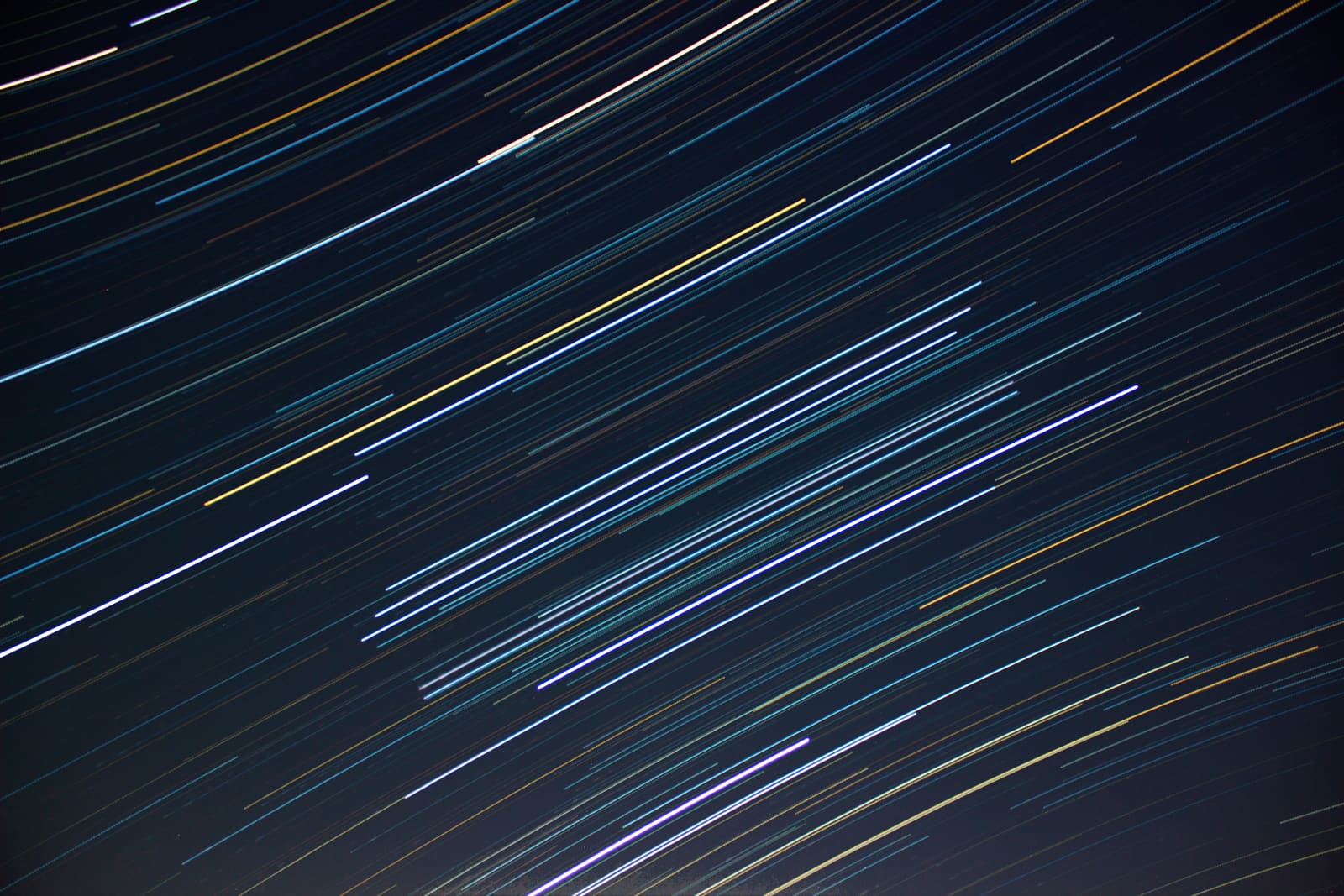 Multiple parallel diagonal star trails in a range of colors, including white, gold, blue, and purple, against a plain black night sky.